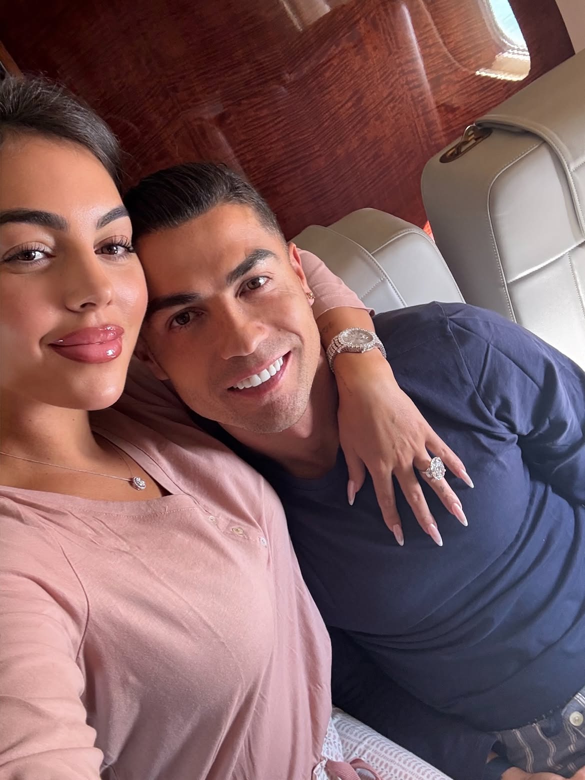Woman and man take a selfie on a private jet; she wears a large oval diamond ring and he wears a jeweled watch.