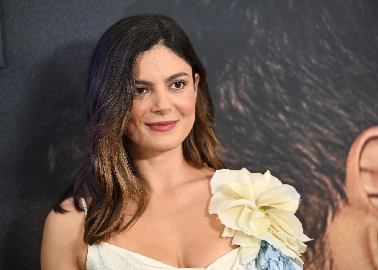 Monica Barbaro in a white dress with a large cream flower detail, smiling at the One Night Only premiere.