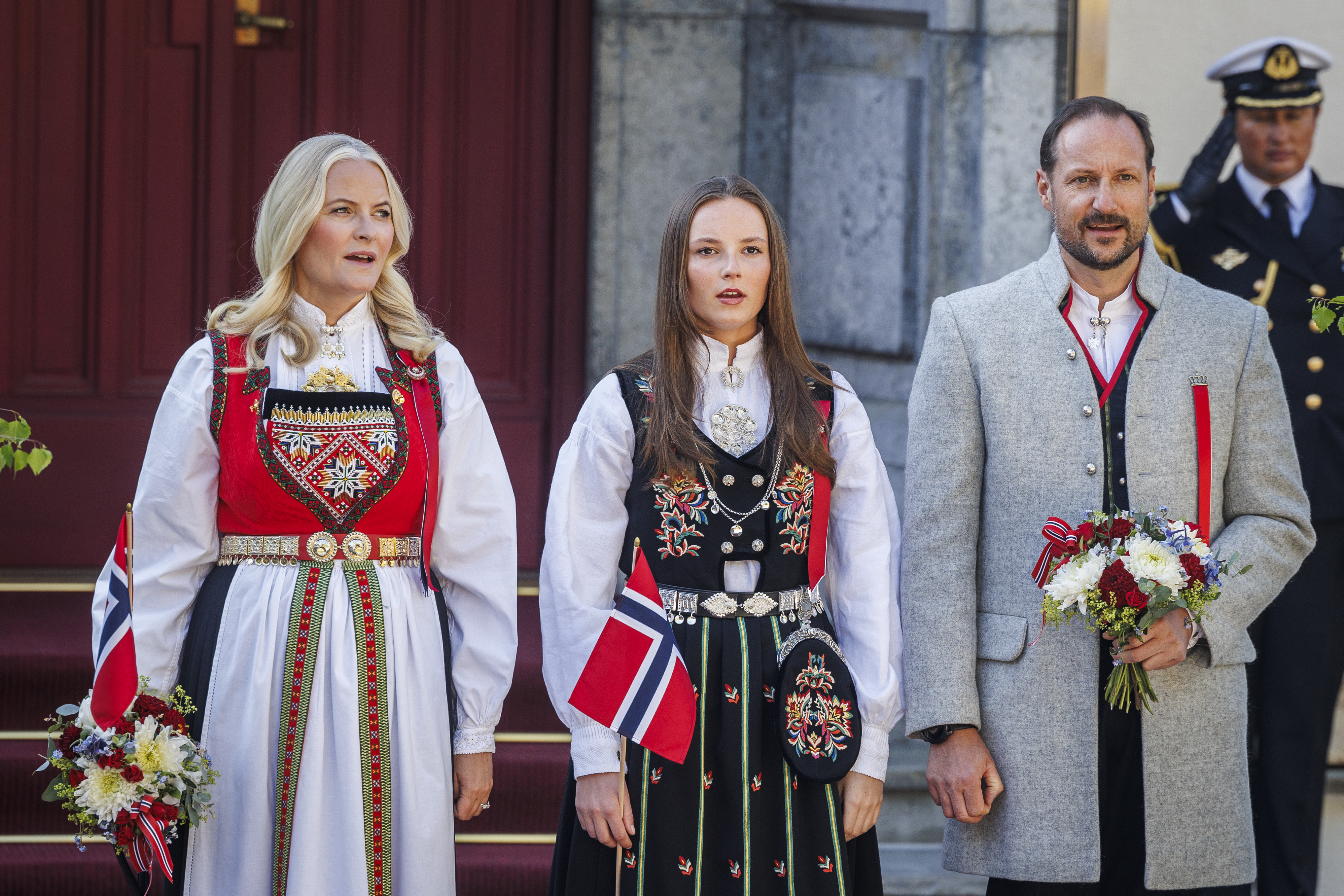 Crown Princess Mette-Marit, Princess Ingrid Alexandra, and Crown Prince Haakon Magnus waving at a children's parade on Norwegian National Day 2024