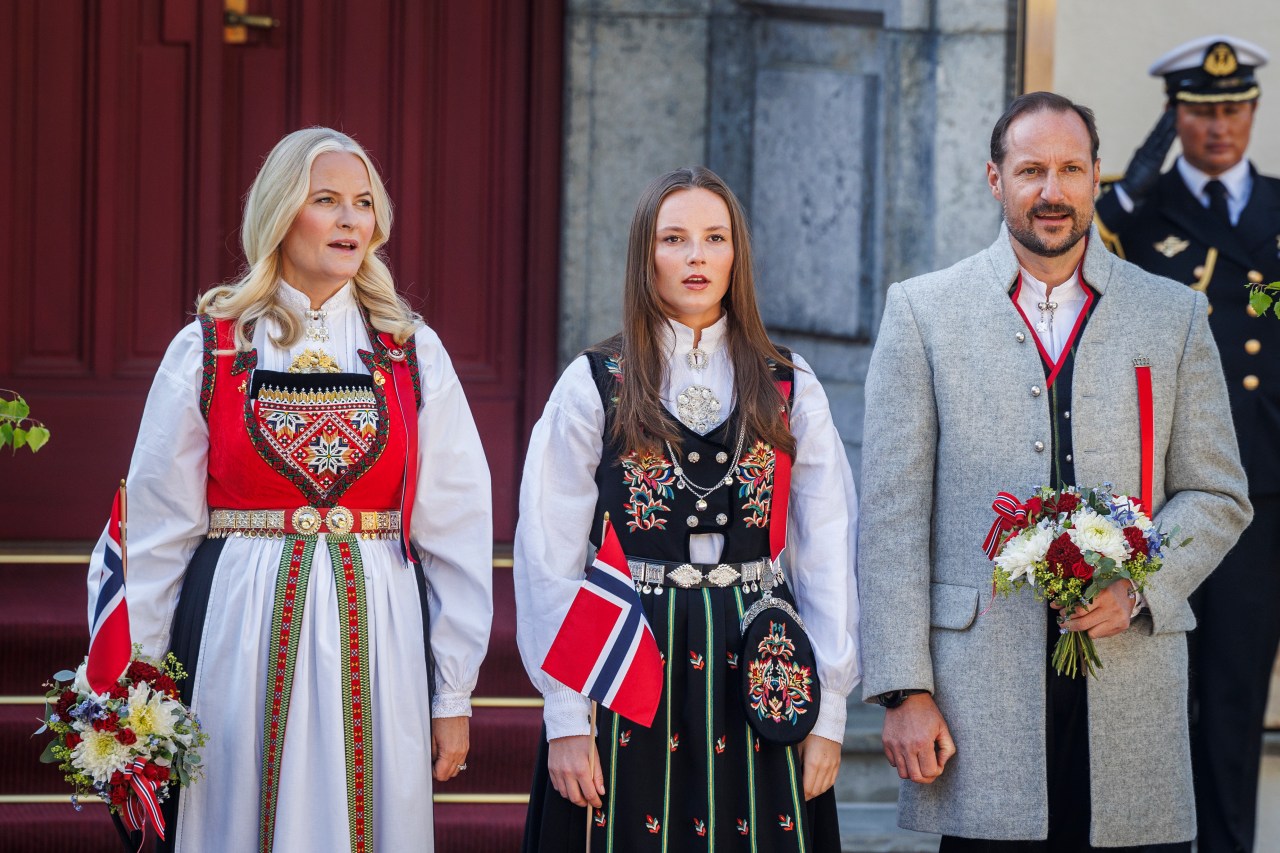 Crown Princess Mette-Marit, Princess Ingrid Alexandra, and Crown Prince Haakon Magnus waving at a children's parade on Norwegian National Day 2024