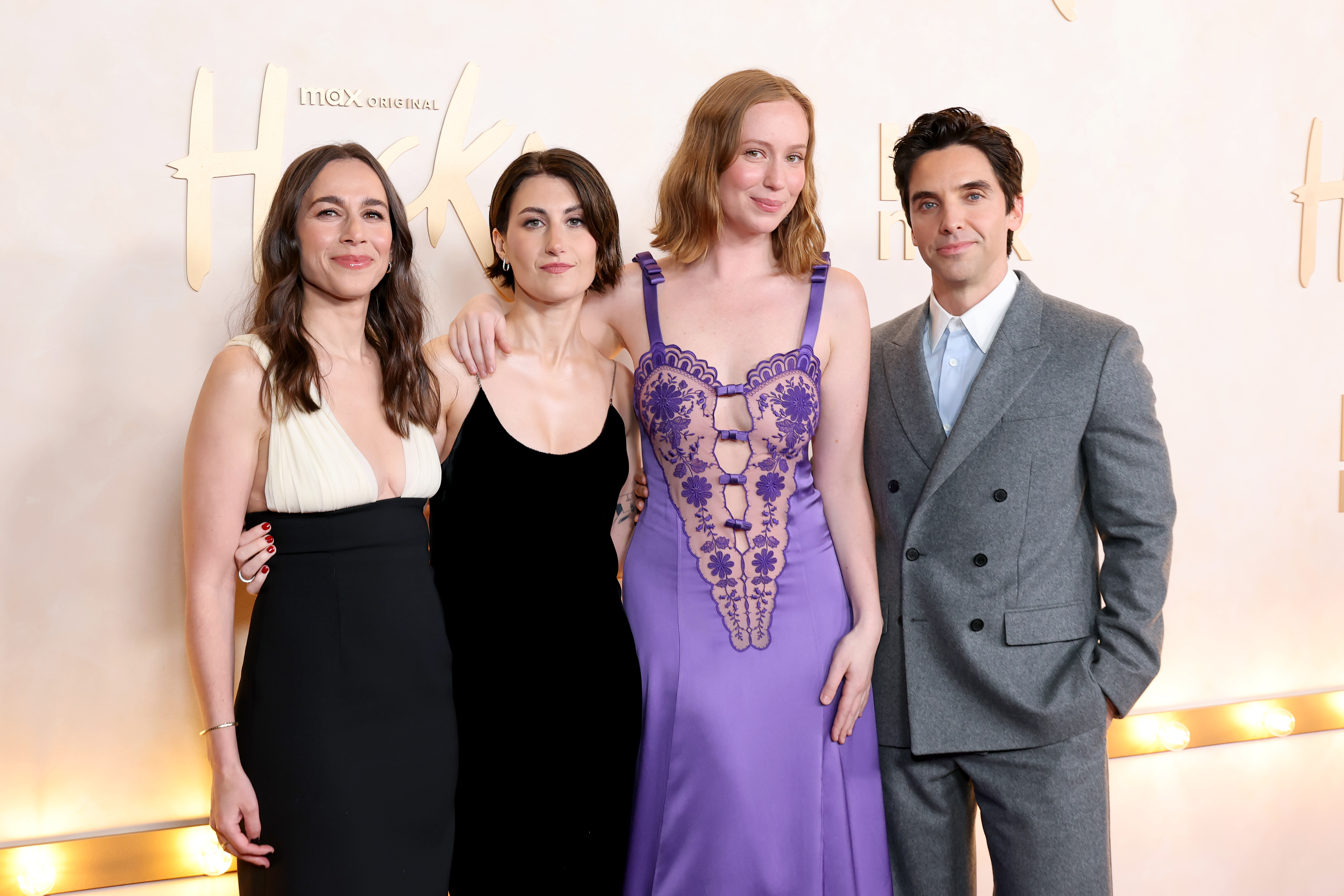 Lucia Aniello, Jen Statsky, Hannah Einbinder, and Paul W. Downs standing together at a Max Original 'Hacks' premiere event backdrop.