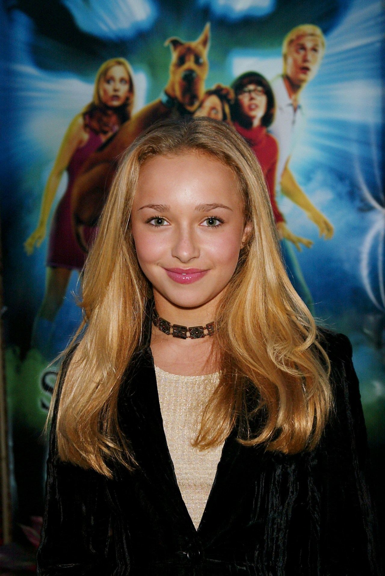Young blonde girl smiling in front of a Scooby-Doo movie poster at a DVD launch event.