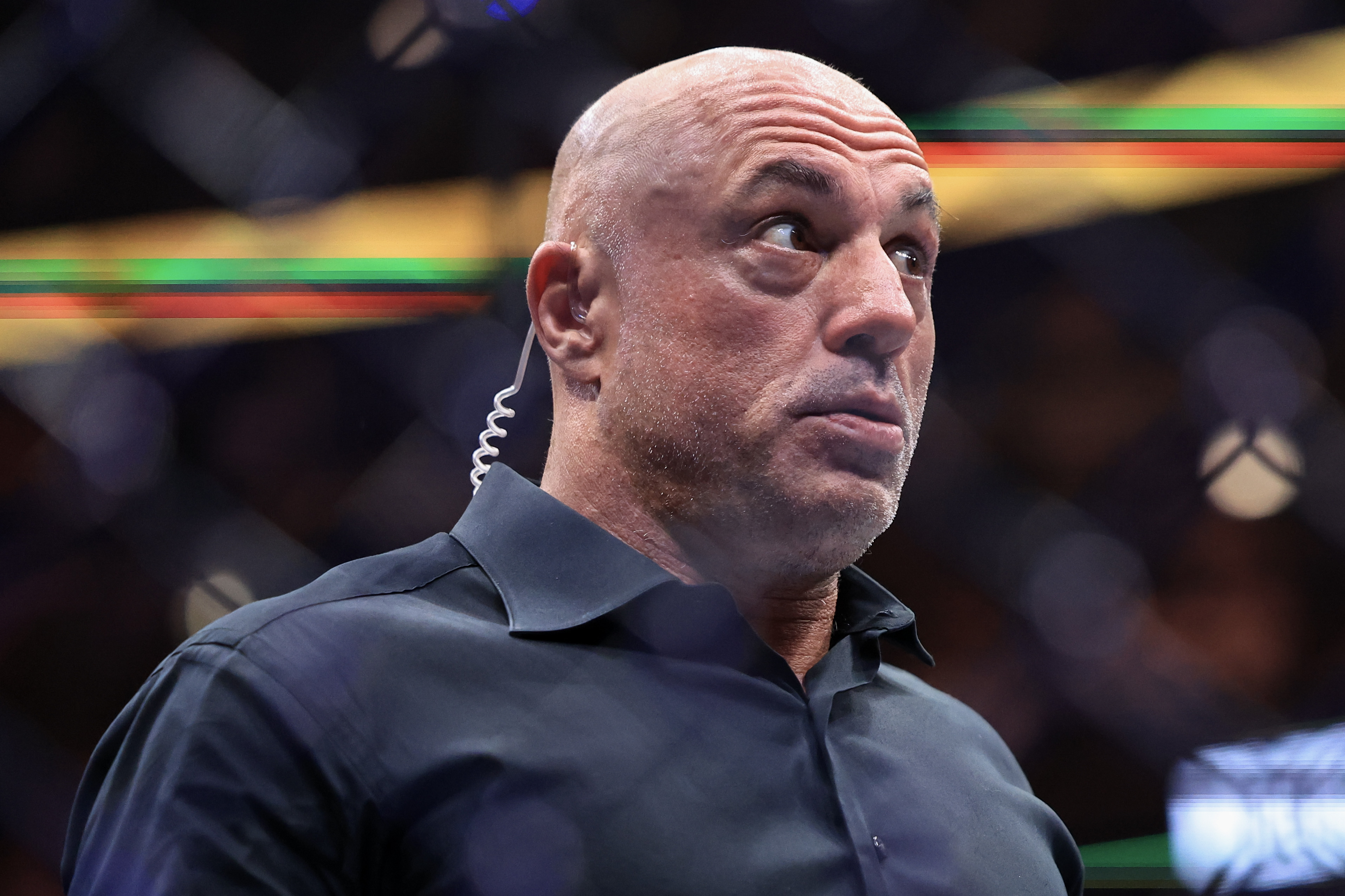 Bald man in a dark shirt with an earpiece looks upward with a surprised expression at a UFC event.