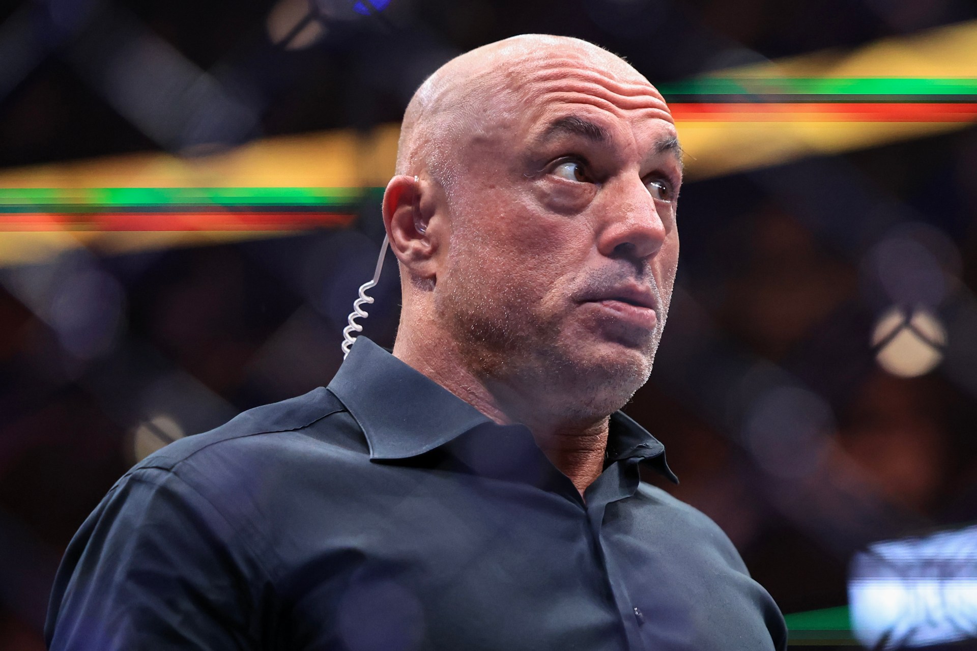 Bald man in a dark shirt with an earpiece looks upward with a surprised expression at a UFC event.