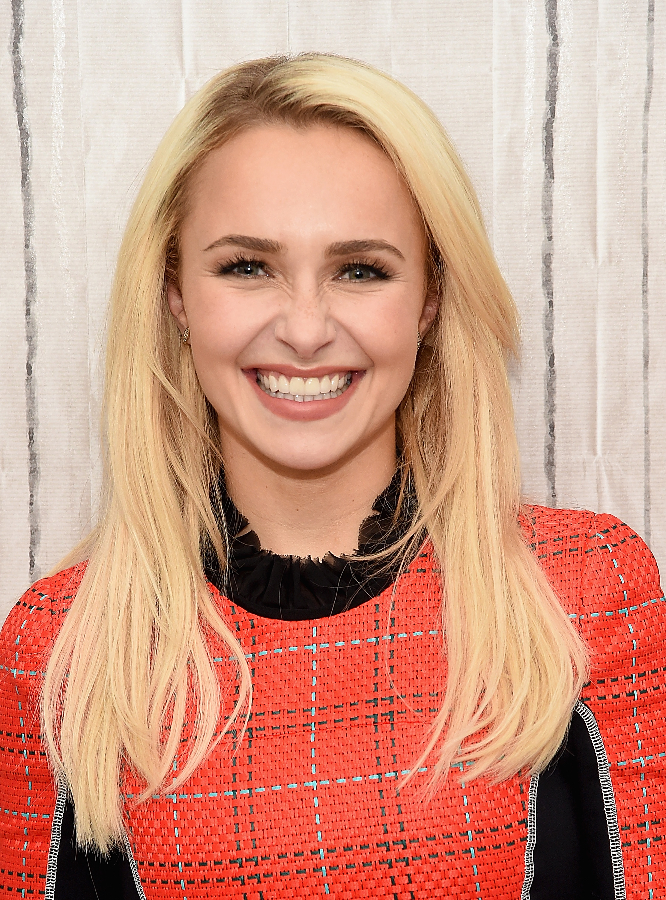 Hayden Panettiere smiling with long blonde hair, wearing a red and black patterned top at a Build Series event.