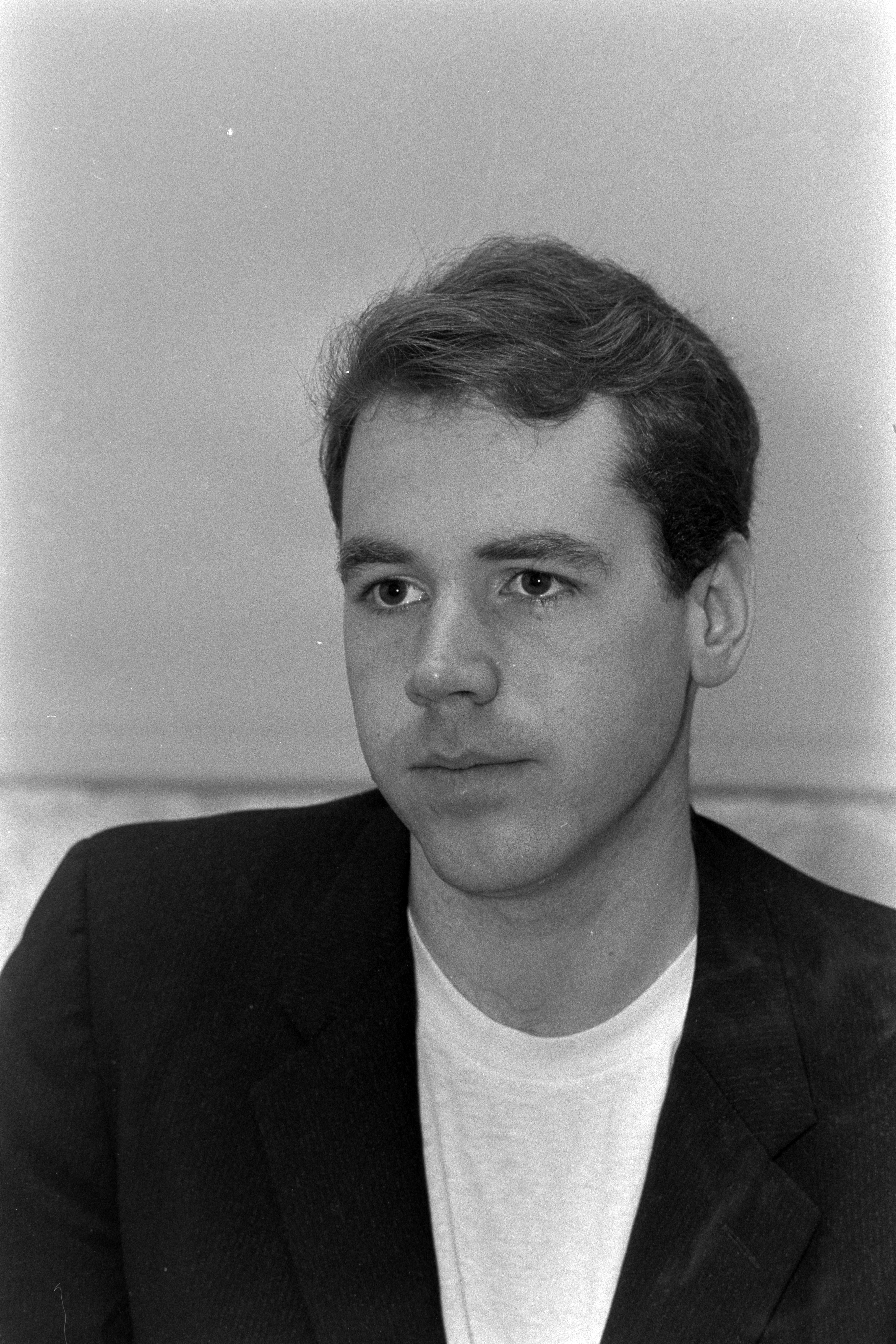 Black-and-white portrait of a young man in a dark blazer and white t-shirt, looking directly at the camera.