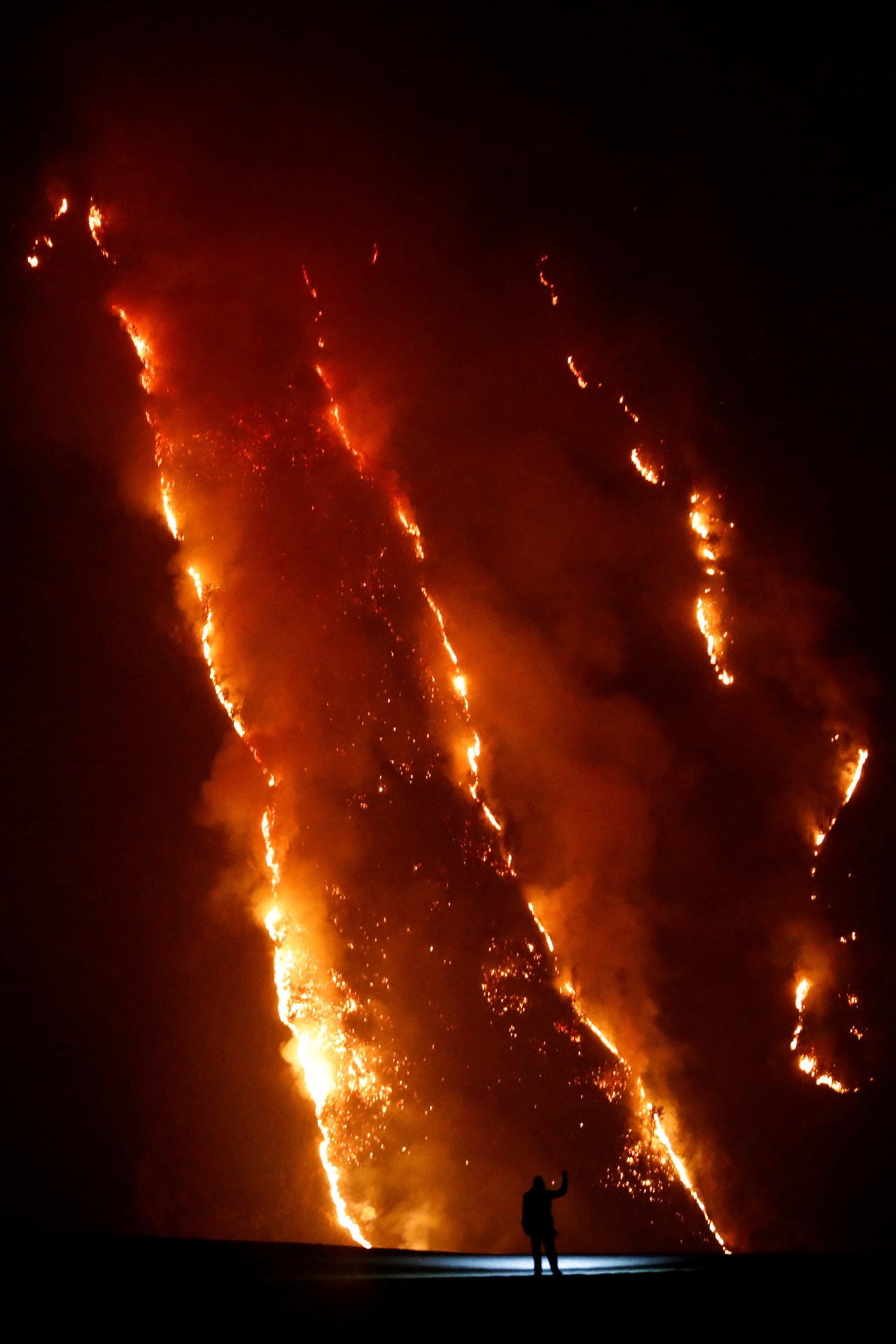 A person standing on a hill watching wildfire flames spread across a slope in Bromo Tengger Semeru National Park, East Java, Indonesia.