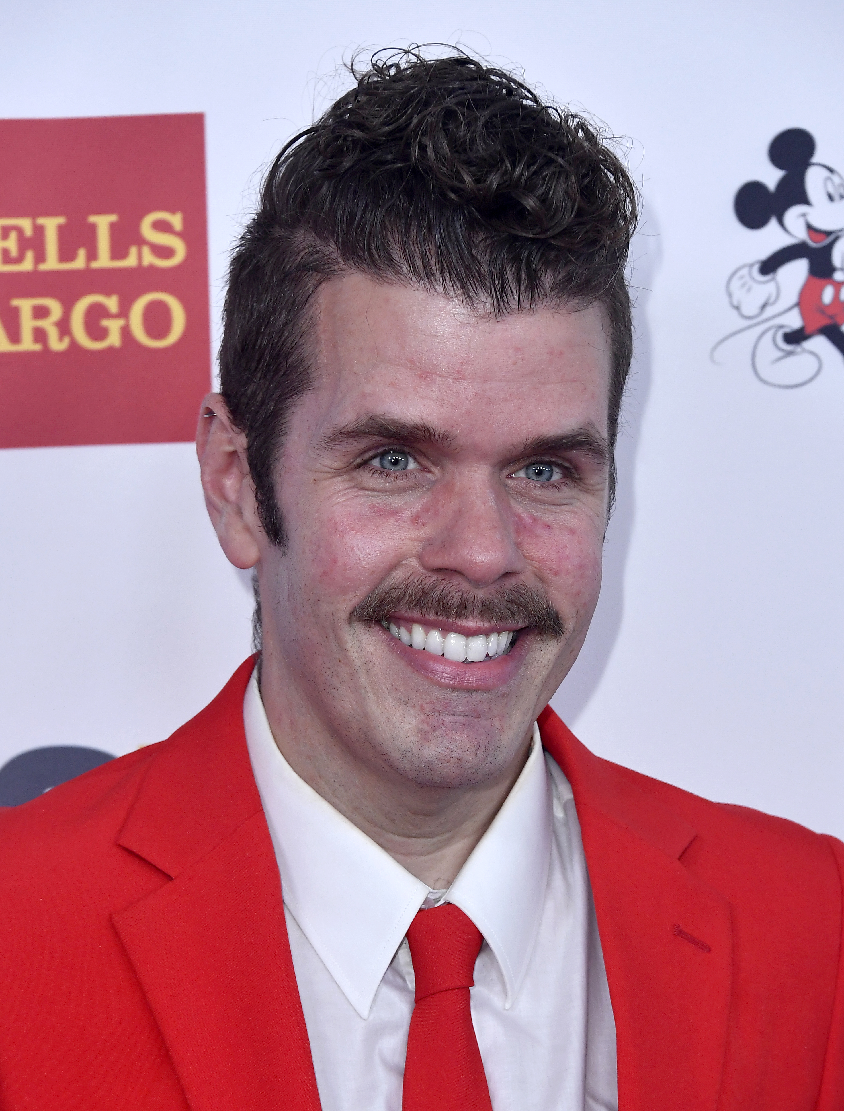 Click to open the image gallery Perez Hilton smiling in a red suit and tie at the 2017 GLSEN Respect Awards in Beverly Hills.