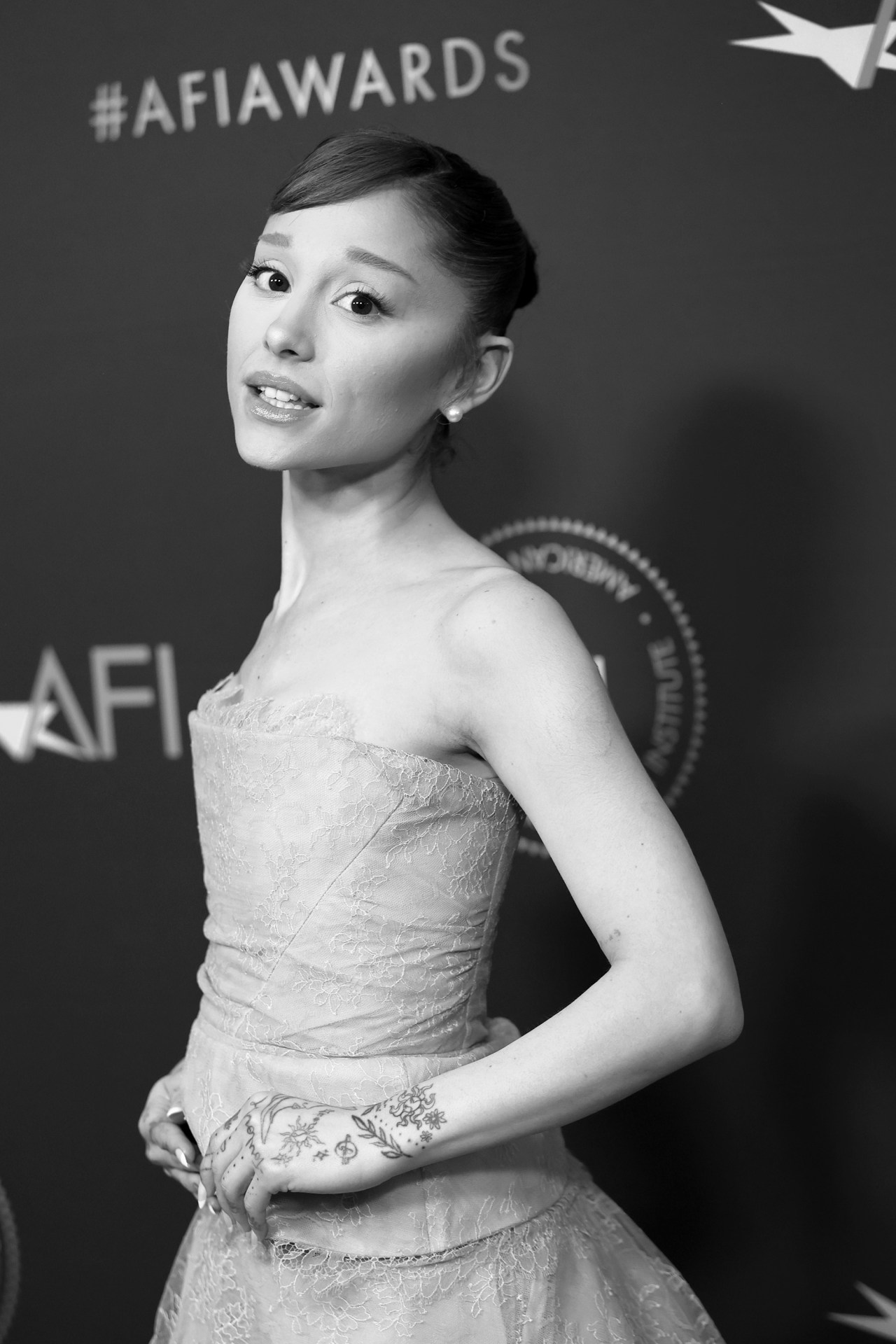 Ariana Grande in a strapless lace dress at the AFI Awards Luncheon, black and white photo, hand tattoos visible