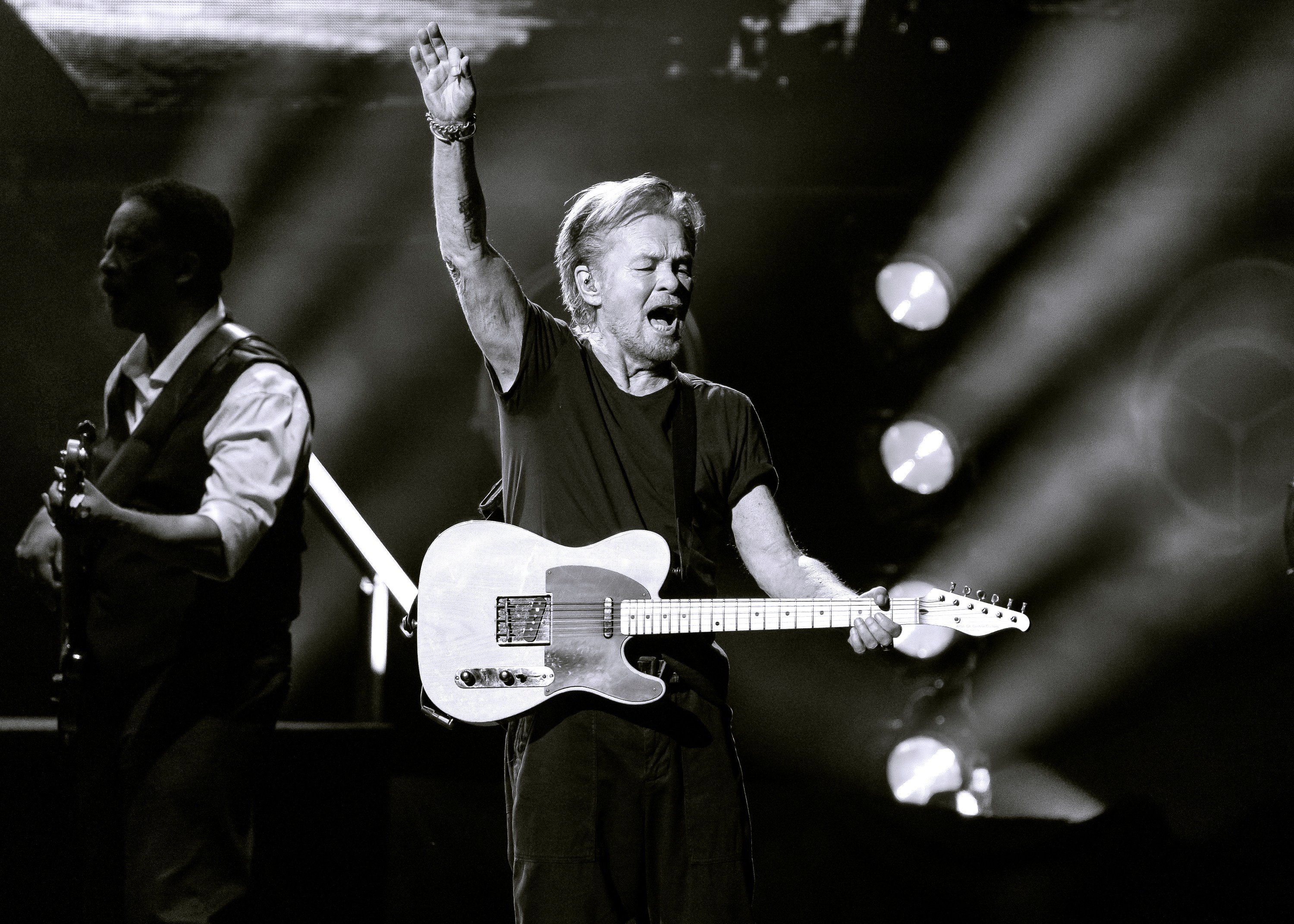 John Mellencamp performing on stage at Acrisure Amphitheater in Grand Rapids, Michigan, in a black and white concert photo