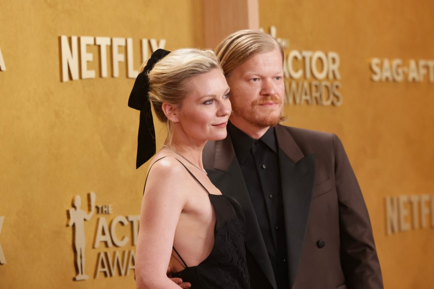 Kirsten Dunst in a black gown with a black bow in her hair stands beside Jesse Plemons in a brown suit at the SAG Awards red carpet.