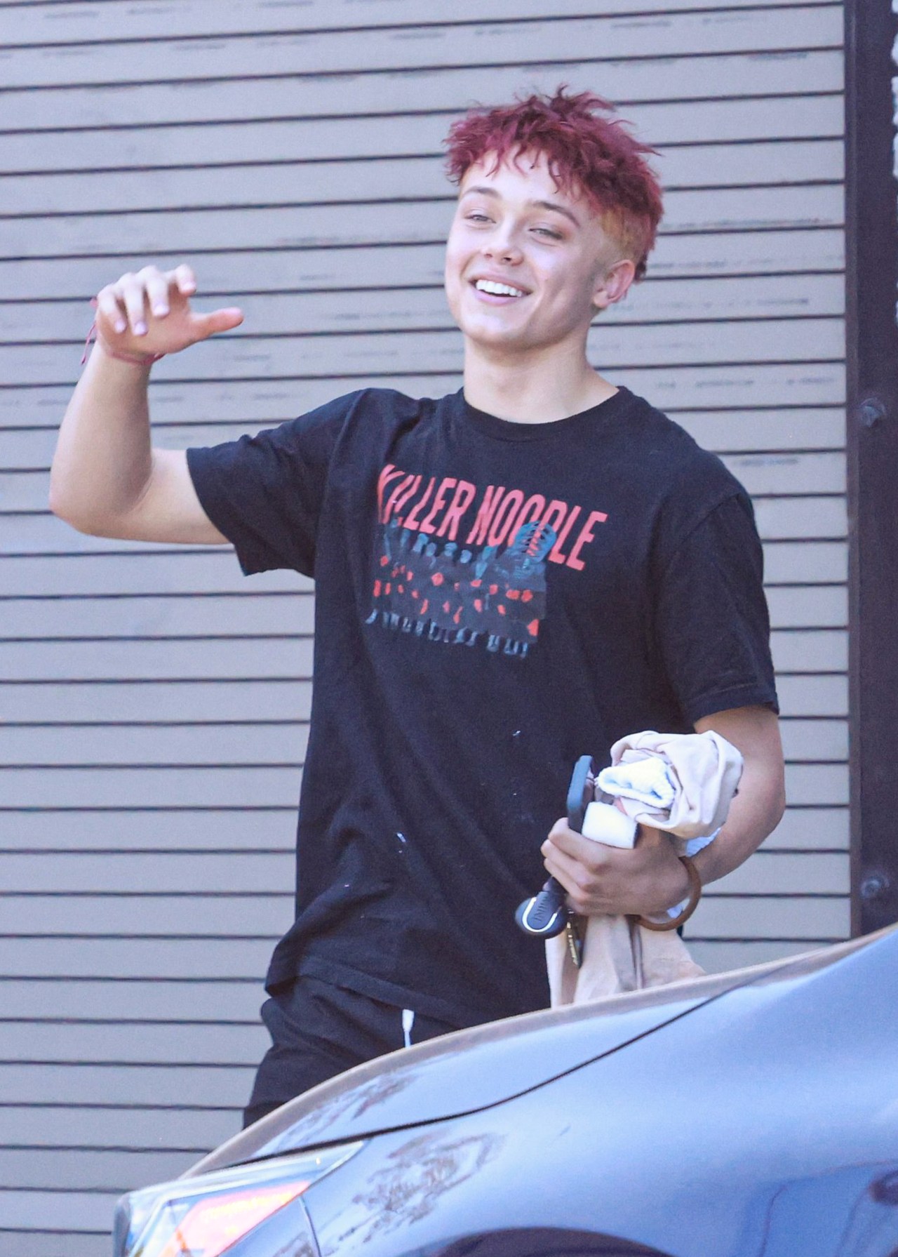 Knox Jolie-Pitt with red hair in a graphic T-shirt, athletic shorts, and pink clogs walking outside after a Muay Thai class