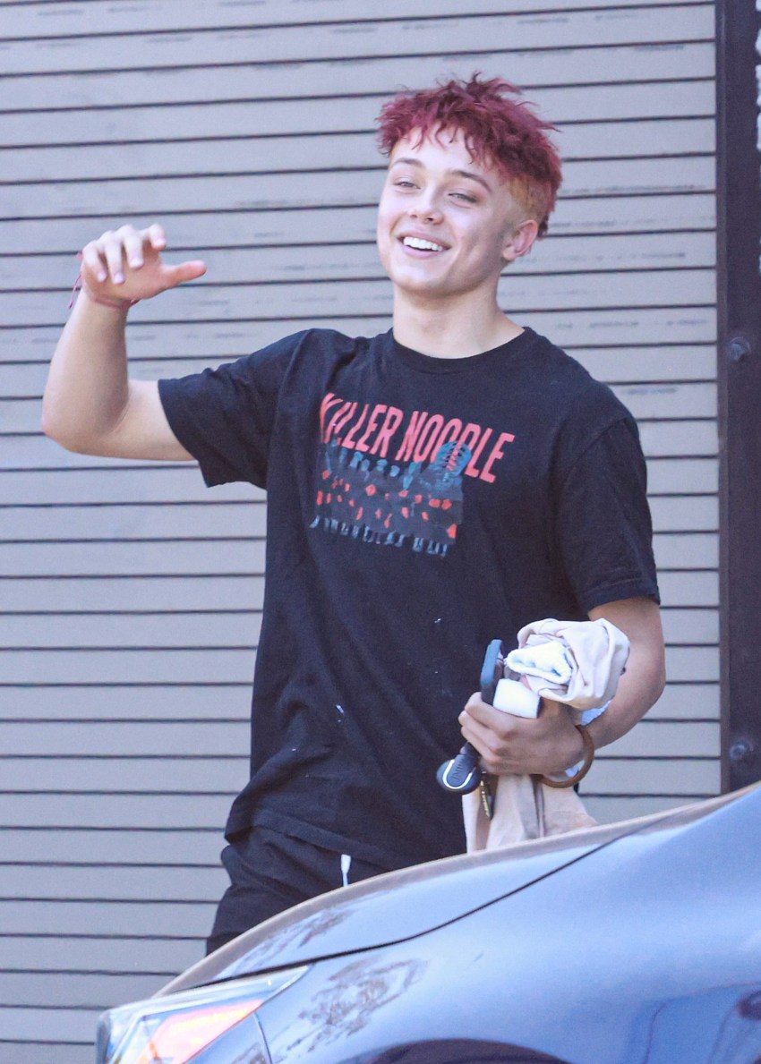 Knox Jolie-Pitt with red hair in a graphic T-shirt, athletic shorts, and pink clogs walking outside after a Muay Thai class
