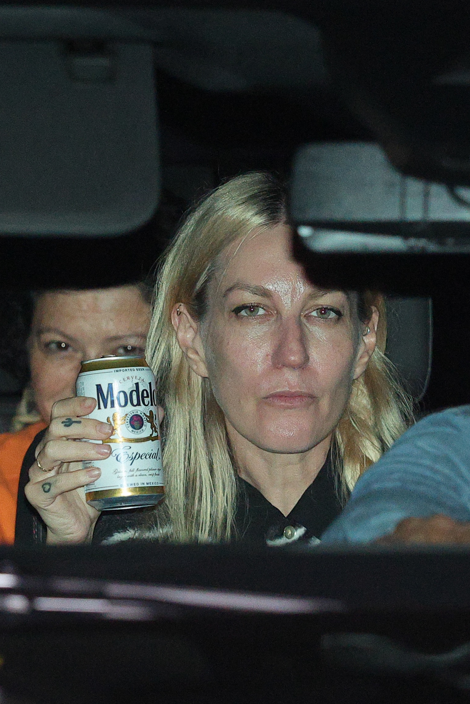 Dylan Meyer holding an open can of Modelo beer in a car alongside Kristen Stewart and Alia Shawkat