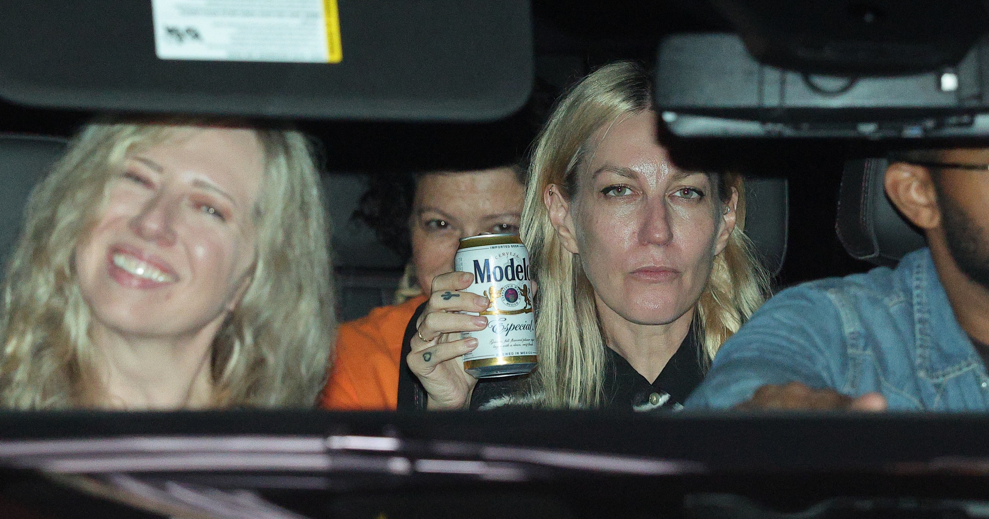 Four people inside a car at night; a blonde woman in the back holds a Modelo Especial beer can while another blonde woman smiles beside her.