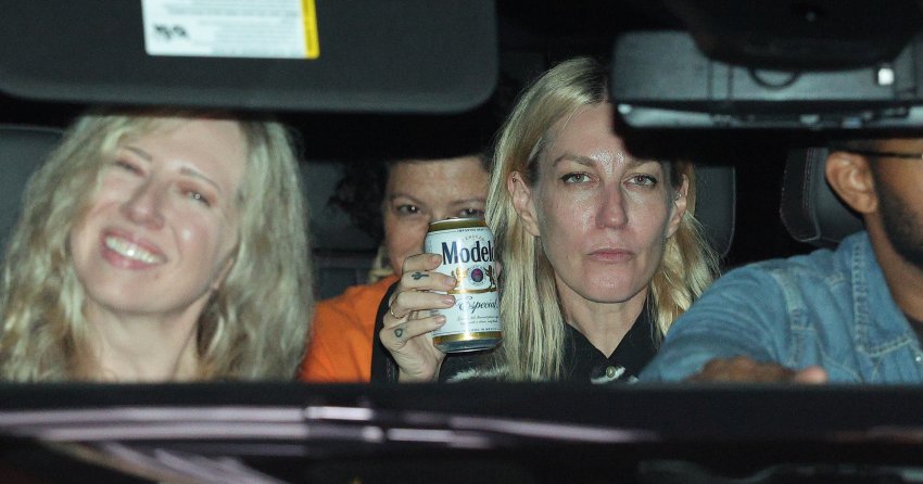 Four people inside a car at night; a blonde woman in the back holds a Modelo Especial beer can while another blonde woman smiles beside her.