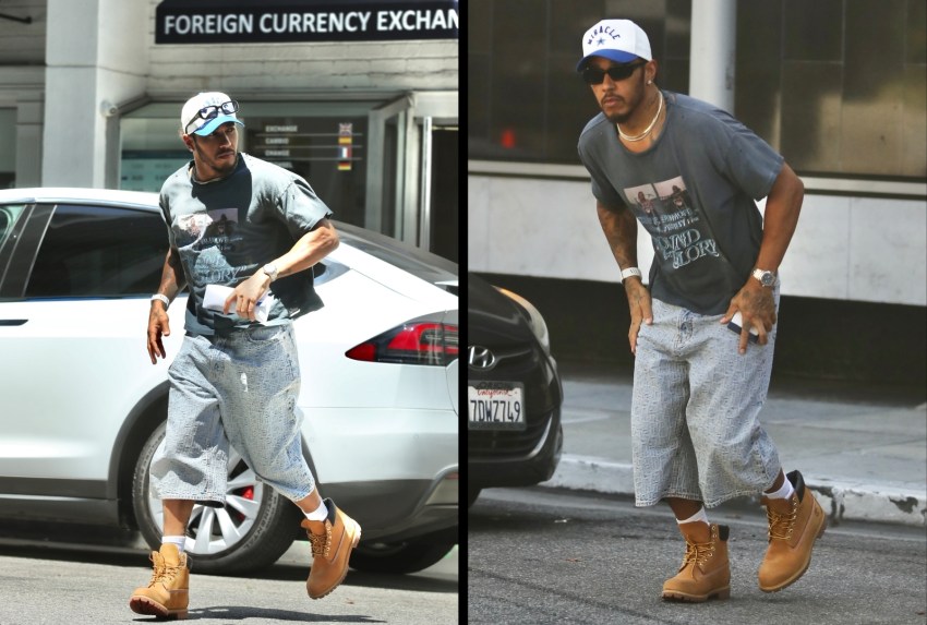 Man in white baseball cap, gray graphic tee, distressed denim shorts, and tan Timberland boots walking across a street in front of a foreign currency exchange.