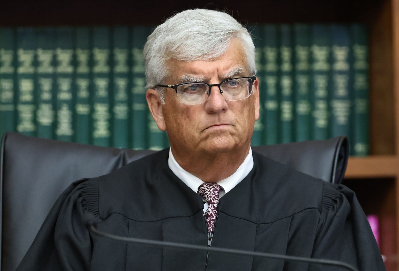 Older man with white hair and glasses wearing a black judicial robe seated at the bench, looking forward with a serious expression.