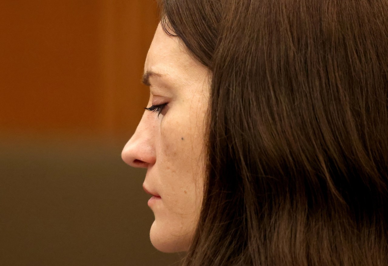 Close-up profile of a dark-haired woman with eyes closed, shot against a blurred warm background in a courtroom.
