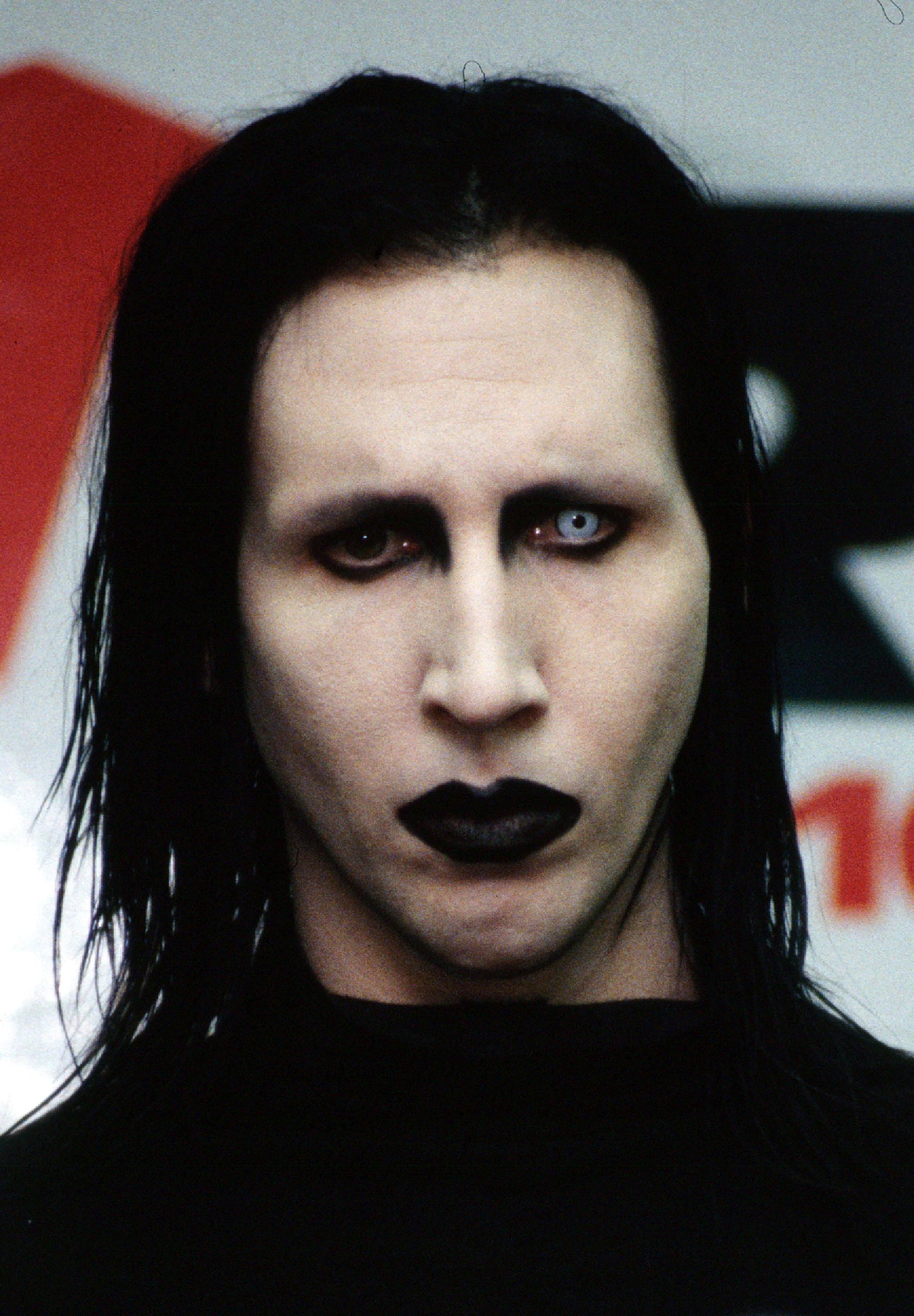 Person with pale white face makeup, black eye makeup, dark lipstick, and long black hair staring intensely at the camera.