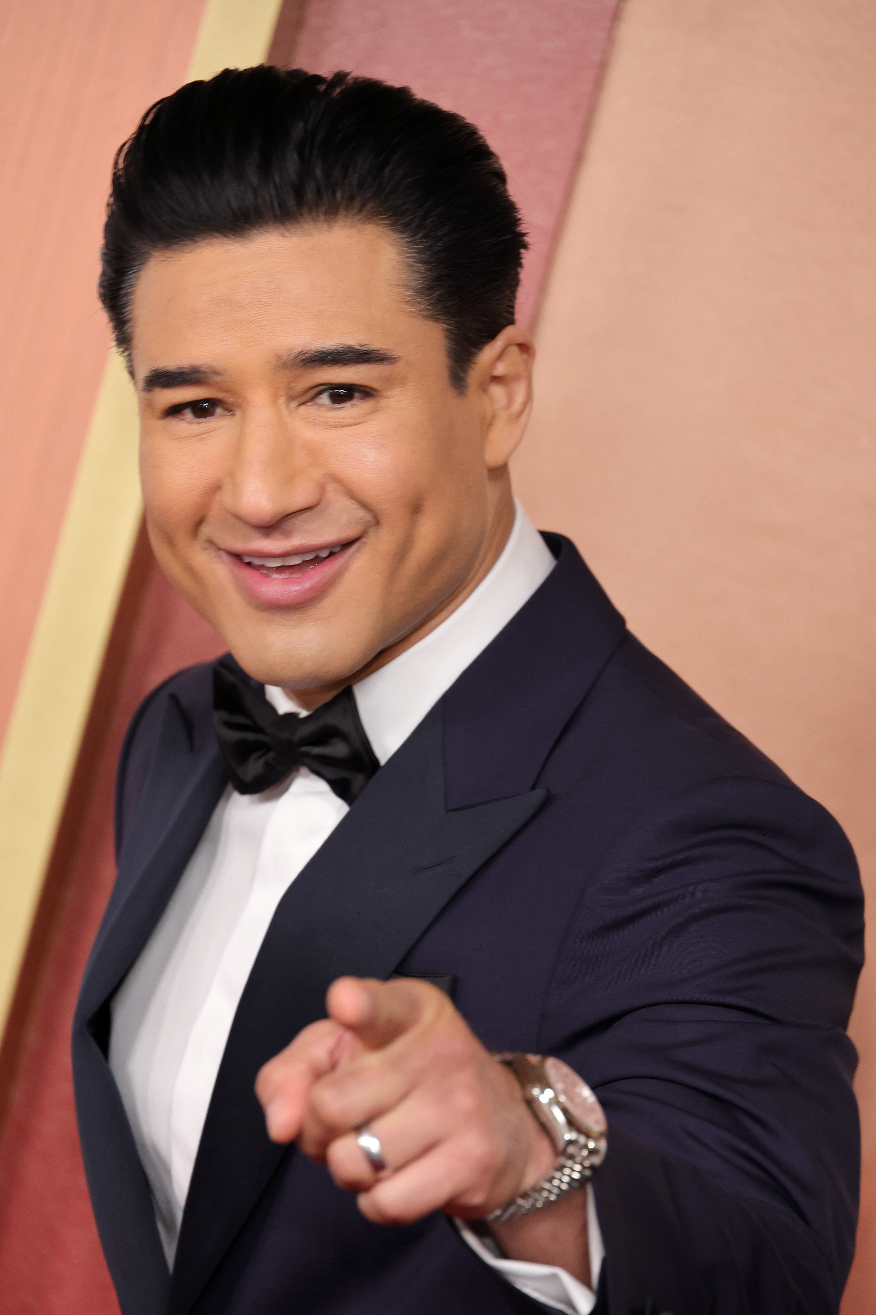 Mario Lopez in a navy tuxedo and black bow tie pointing at the camera and smiling at the 97th Annual Oscars arrivals.