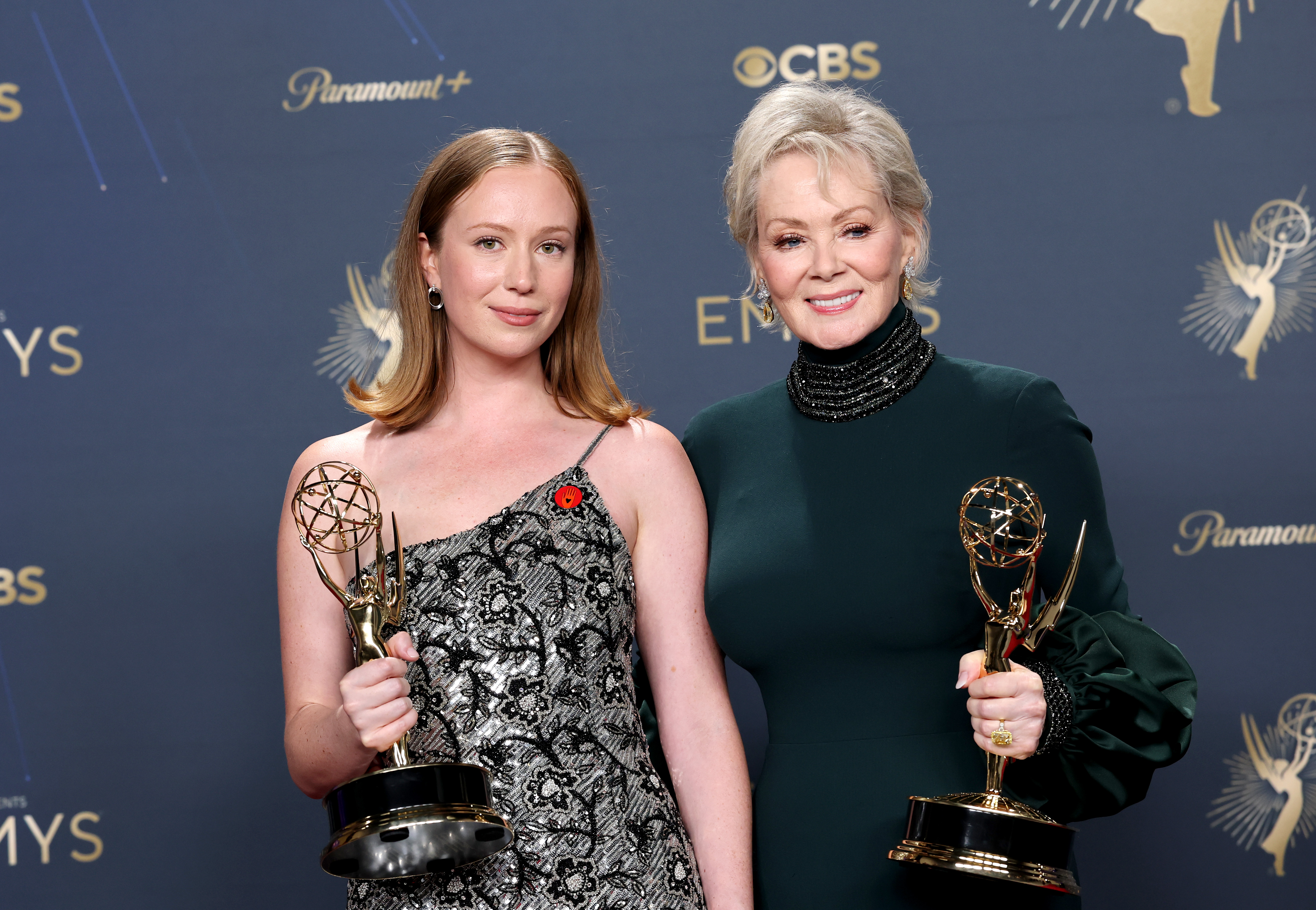 Hannah Einbinder and Jean Smart posing together in the Emmy Awards press room, each holding a trophy.