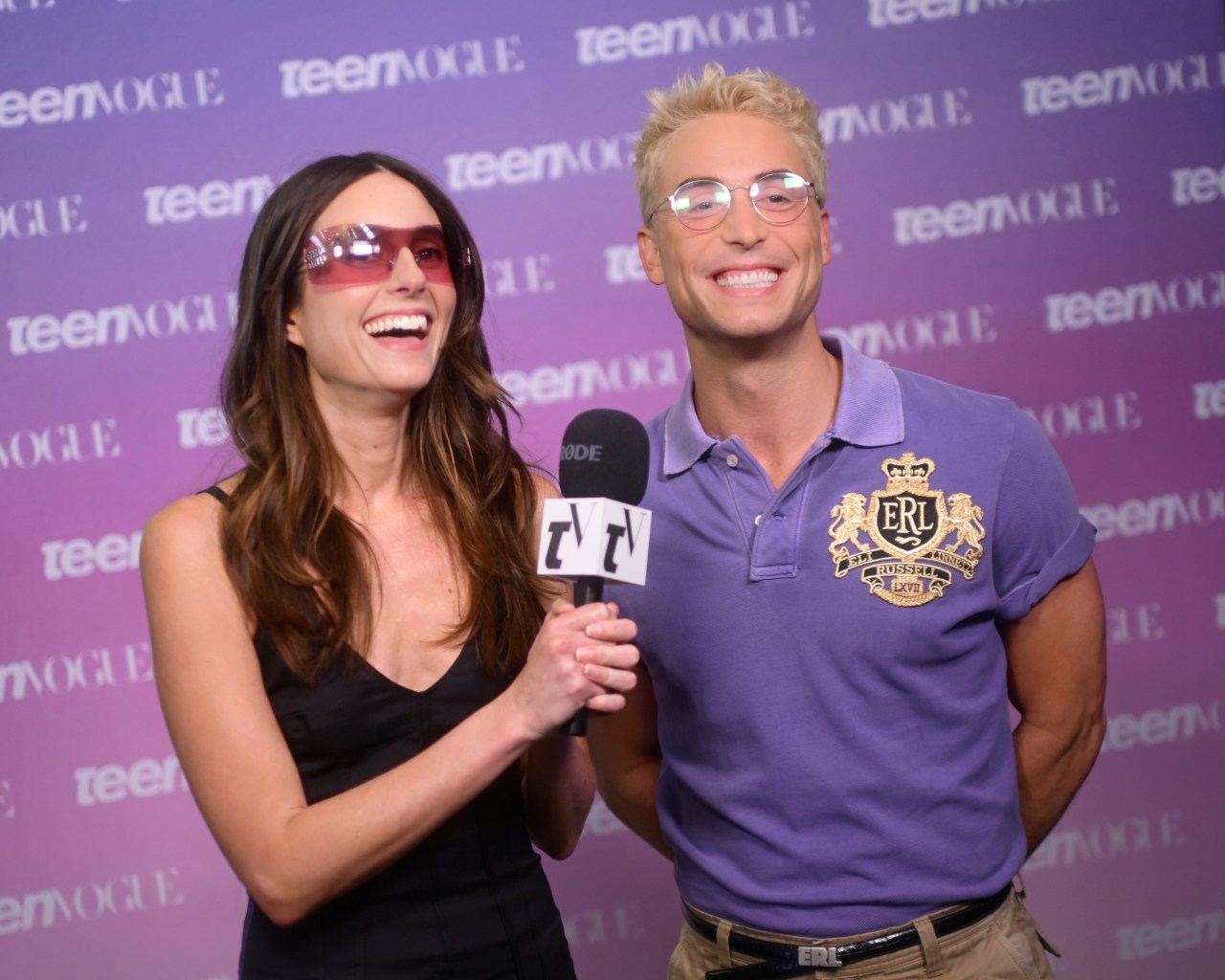 Mary Beth Barone and Benito Skinner smile and laugh together in front of a Teen Vogue step-and-repeat backdrop, sharing a microphone.