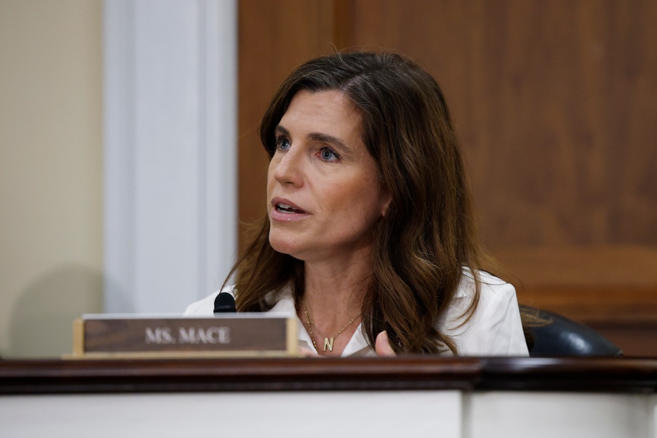 Rep. Nancy Mace speaks at a congressional committee hearing, seated behind a nameplate reading 'Ms. Mace,' wearing a white blazer.