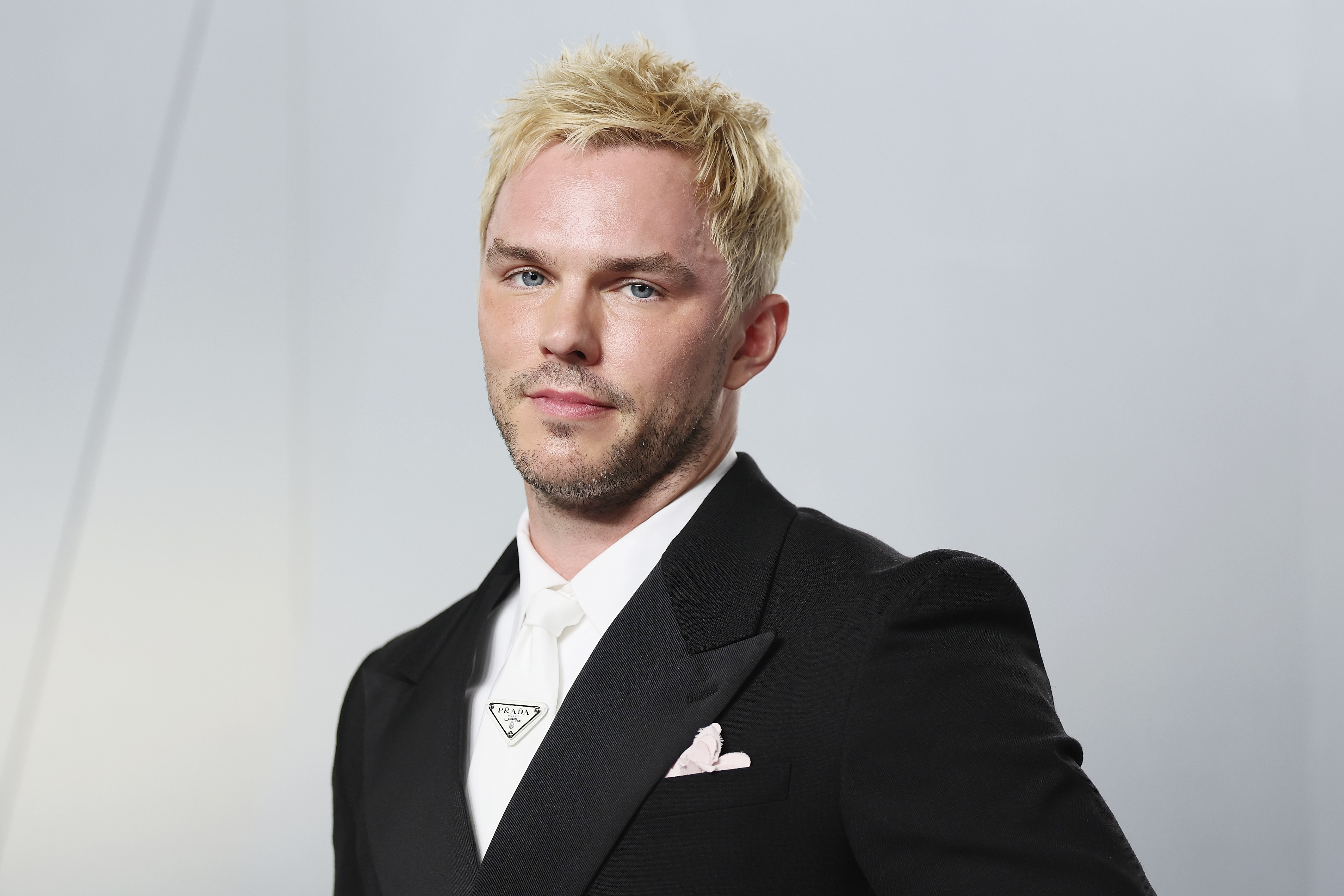 Nicholas Hoult in a black tuxedo with white tie and Prada lapel pin at the 2026 Vanity Fair Oscar Party in Los Angeles.