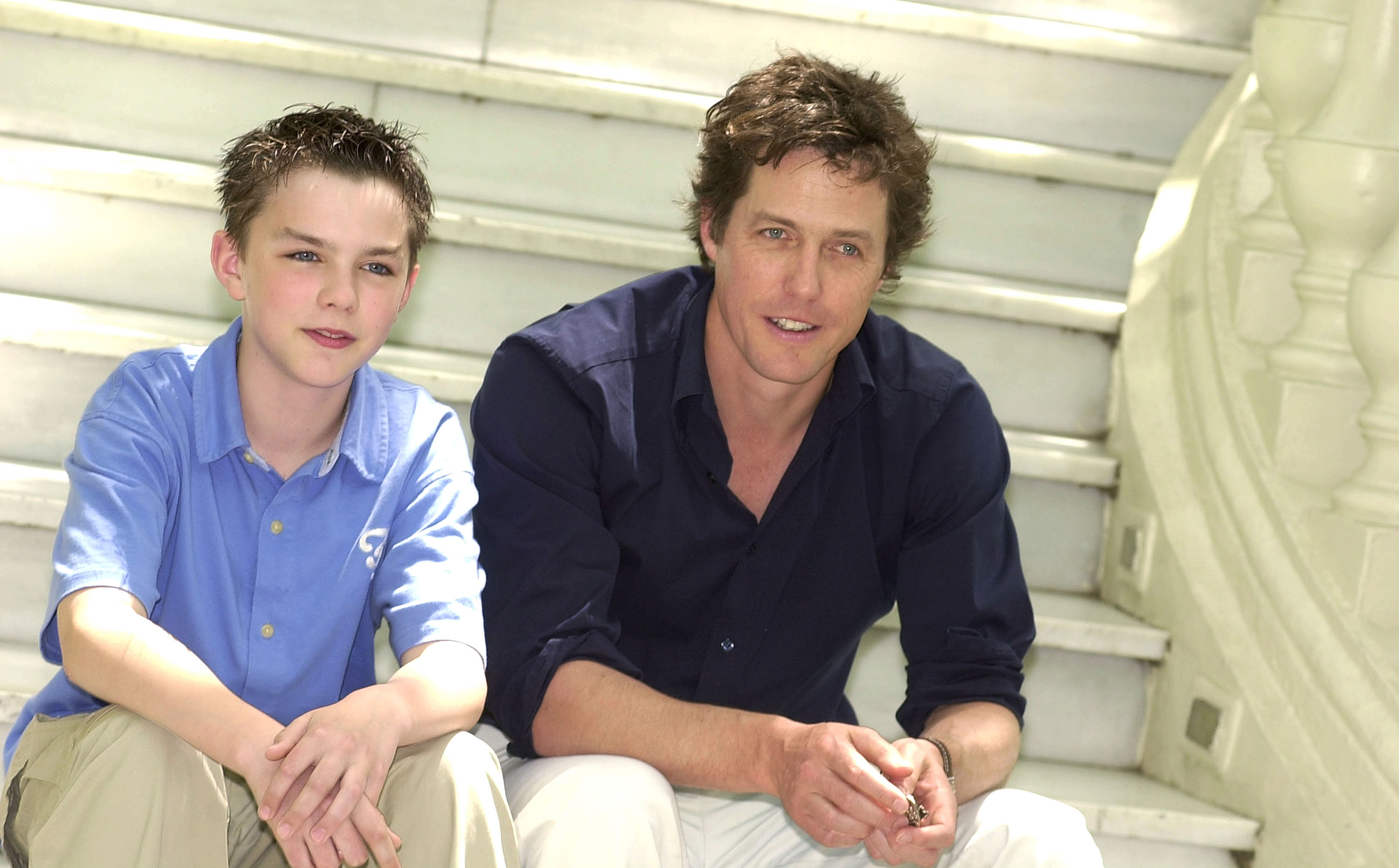 Young boy and an adult man sitting together on white steps, both smiling at the camera.