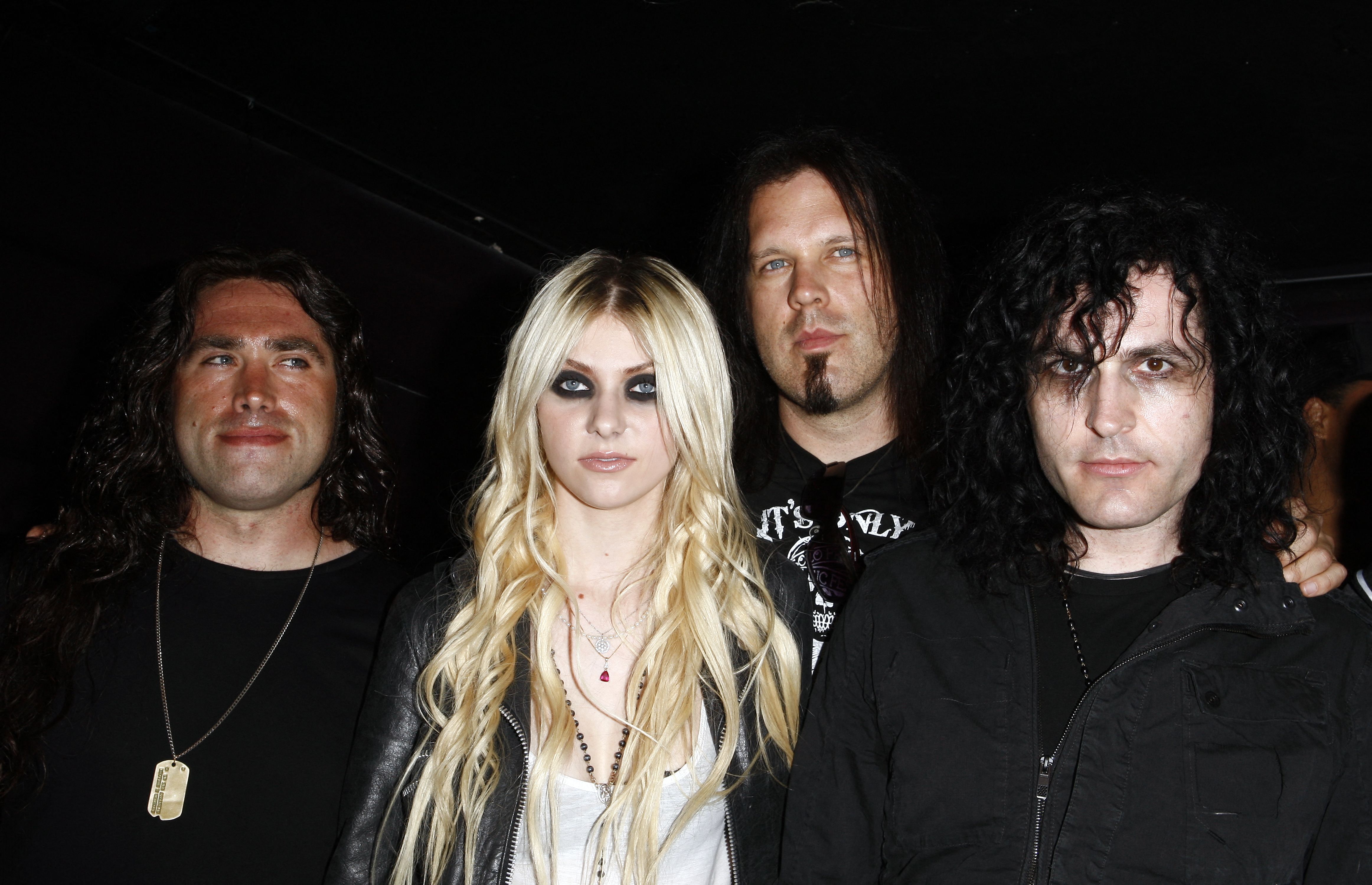Taylor Momsen with long blonde hair and dark eye makeup standing with three male bandmates from The Pretty Reckless, all dressed in black.