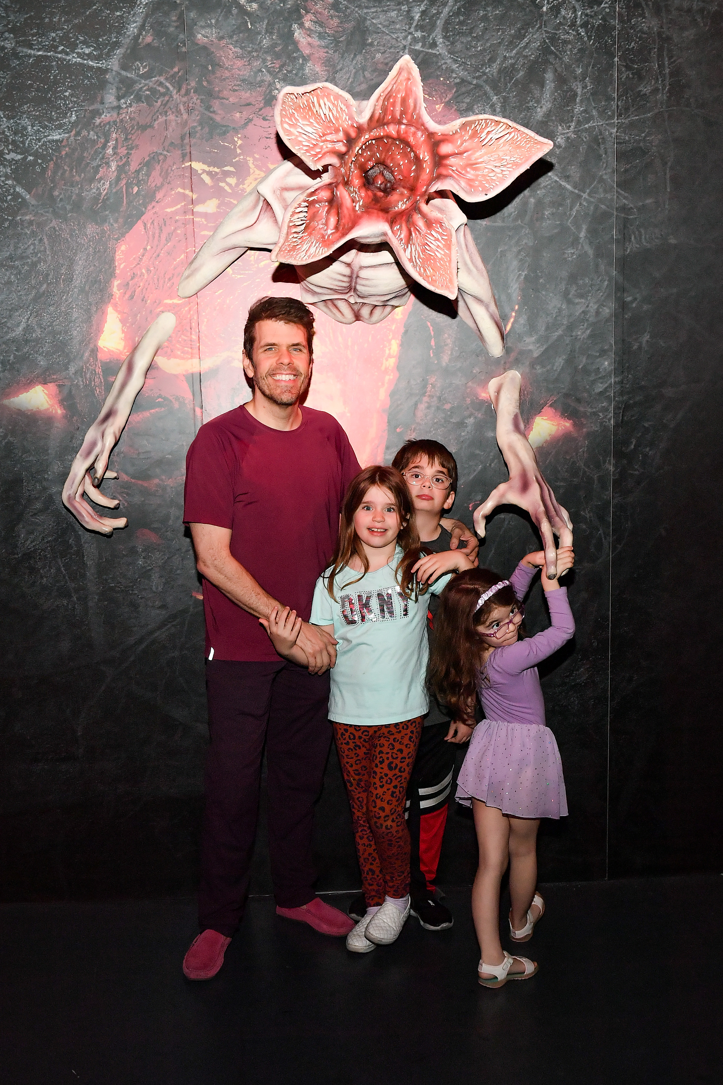 A man and three young children smiling in front of a large Stranger Things Demogorgon monster prop at a Netflix store event.
