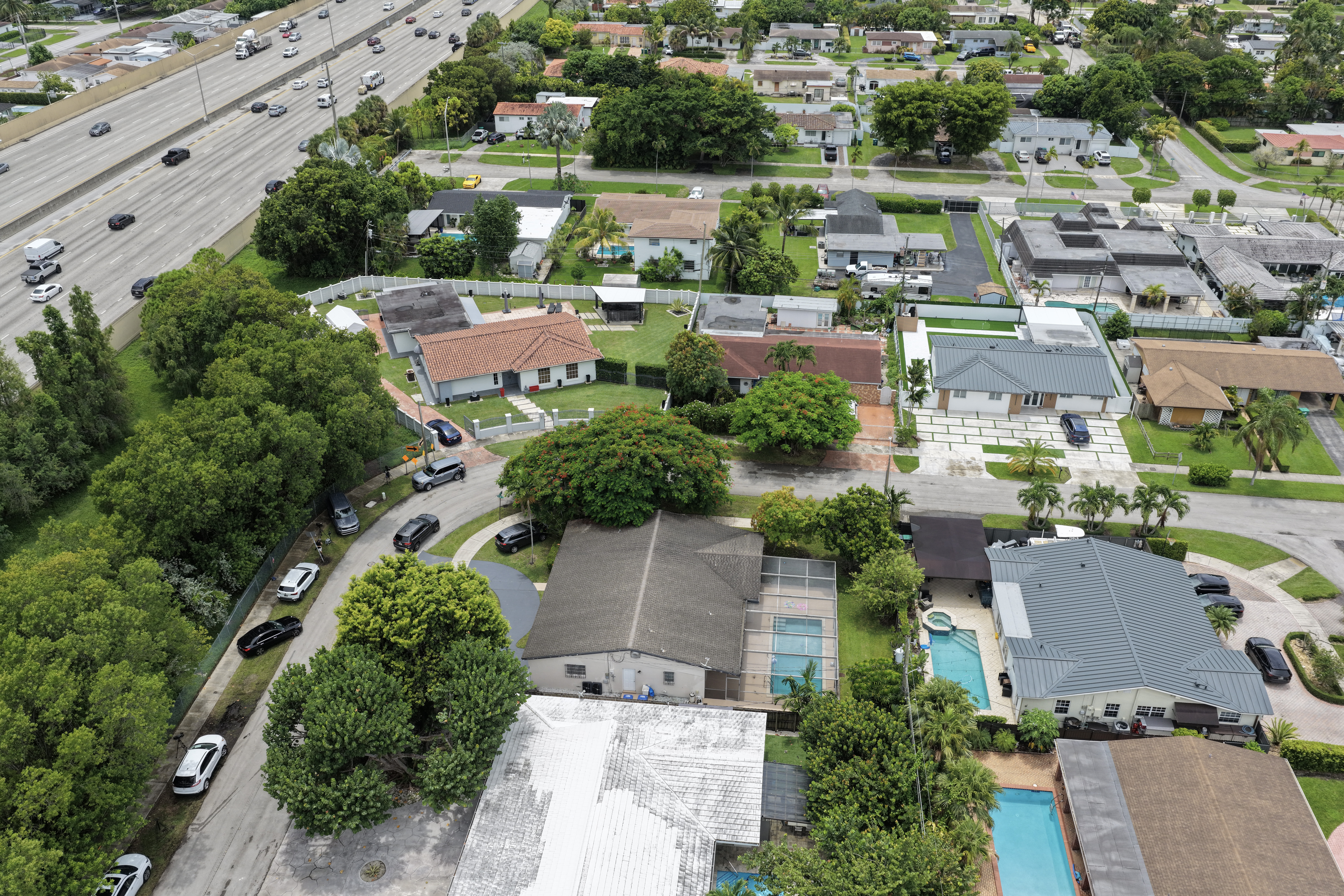 Aerial view of a suburban Florida neighborhood with single-family homes and pools; one house with a gray roof and pool is visible at lower left.