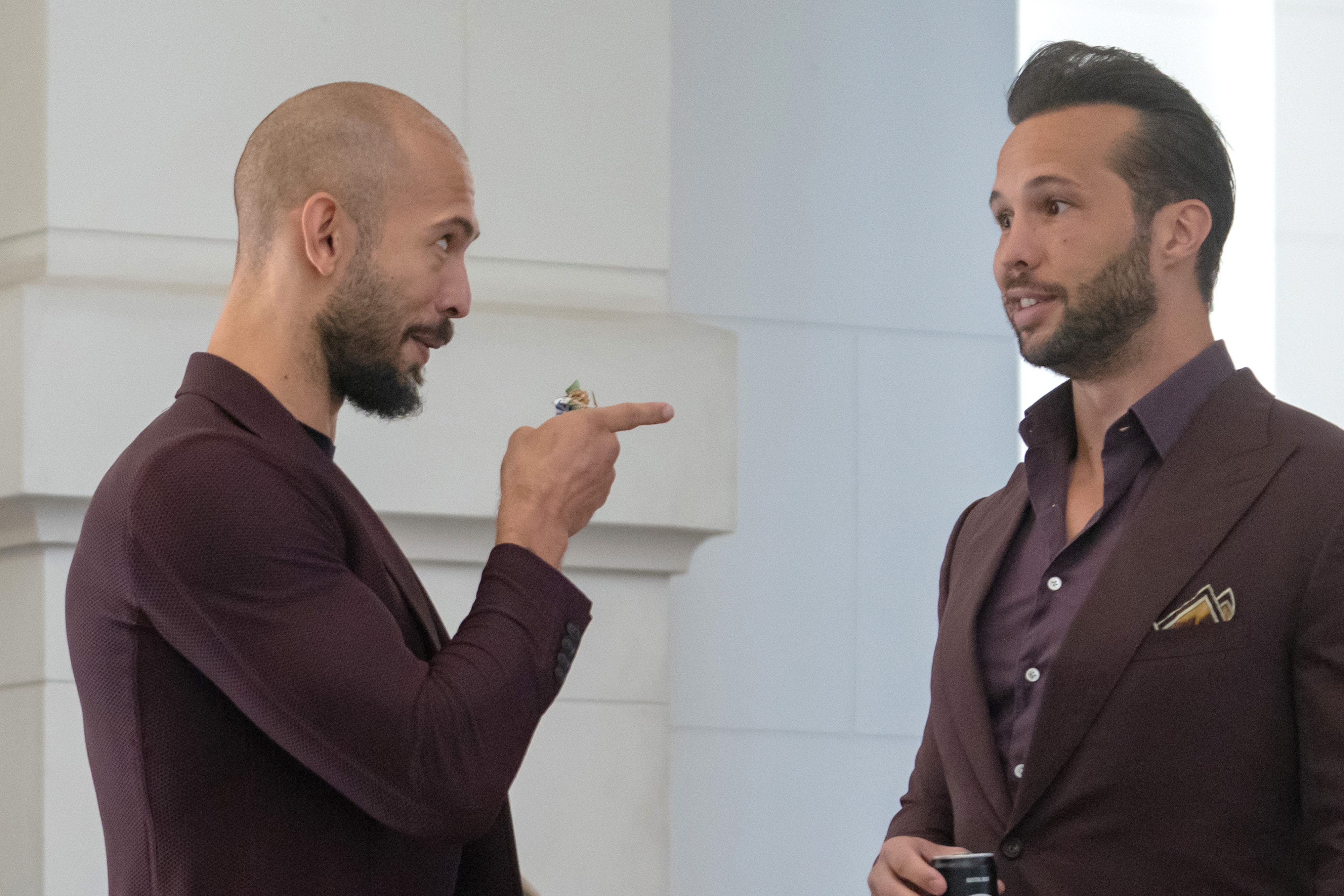 Bald man in burgundy jacket pointing a finger at a bearded man in a dark suit jacket inside a courthouse.