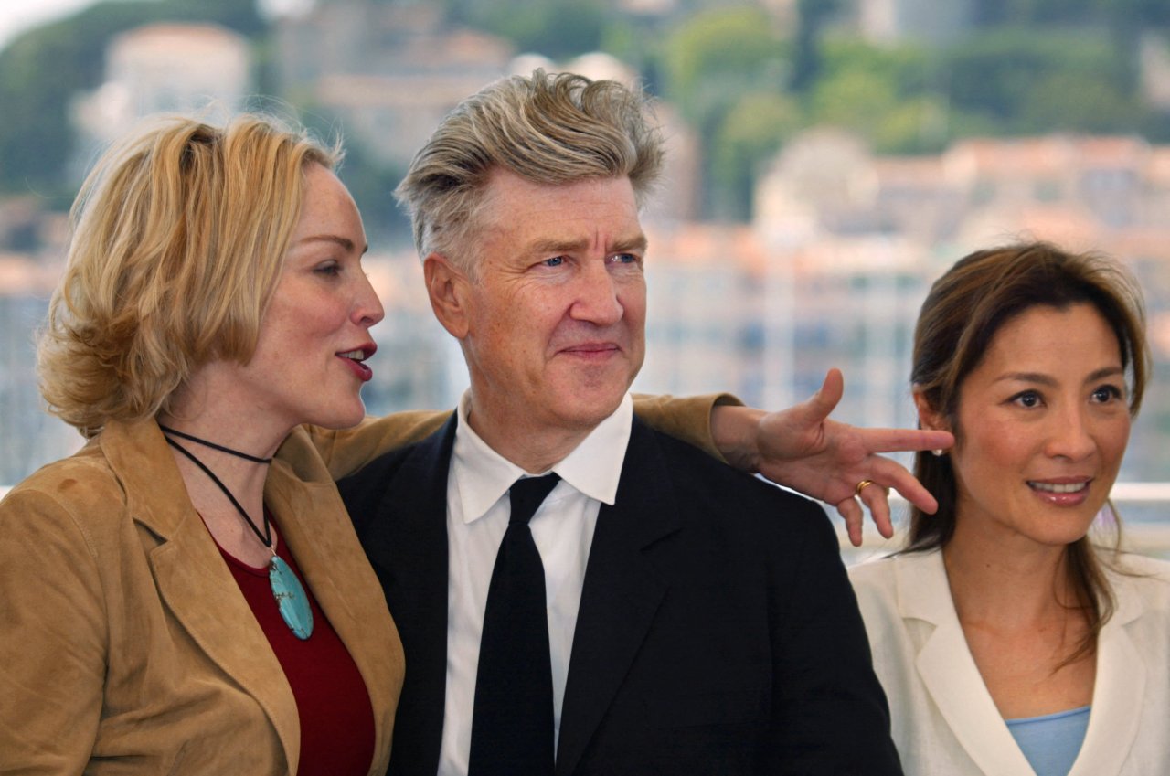 Sharon Stone, David Lynch, and Michelle Yeoh posing together on a terrace at the Cannes Film Festival, 2002.