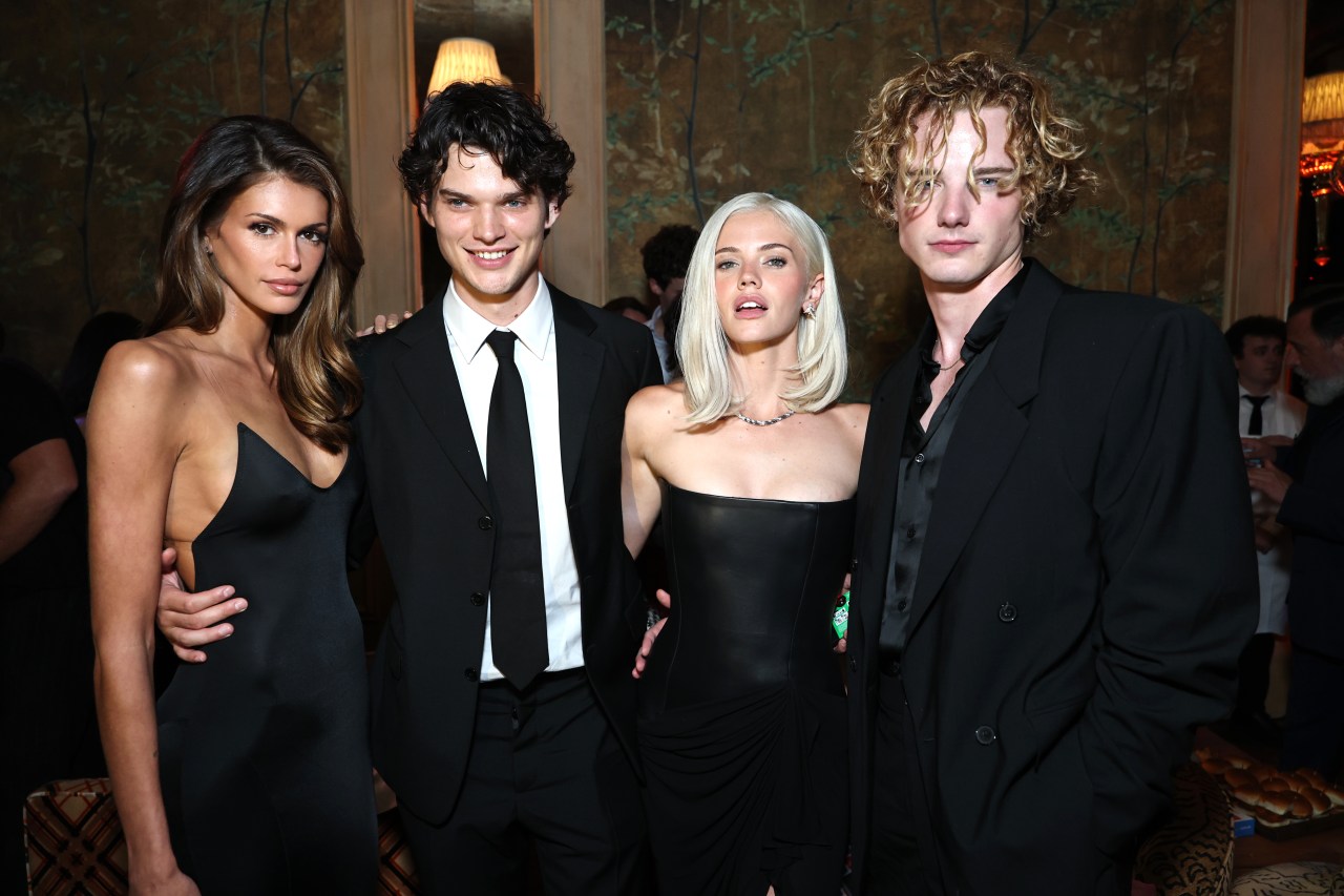 Four young people in black formalwear posing together at an indoor event; two women and two men, one woman with platinum blonde hair.