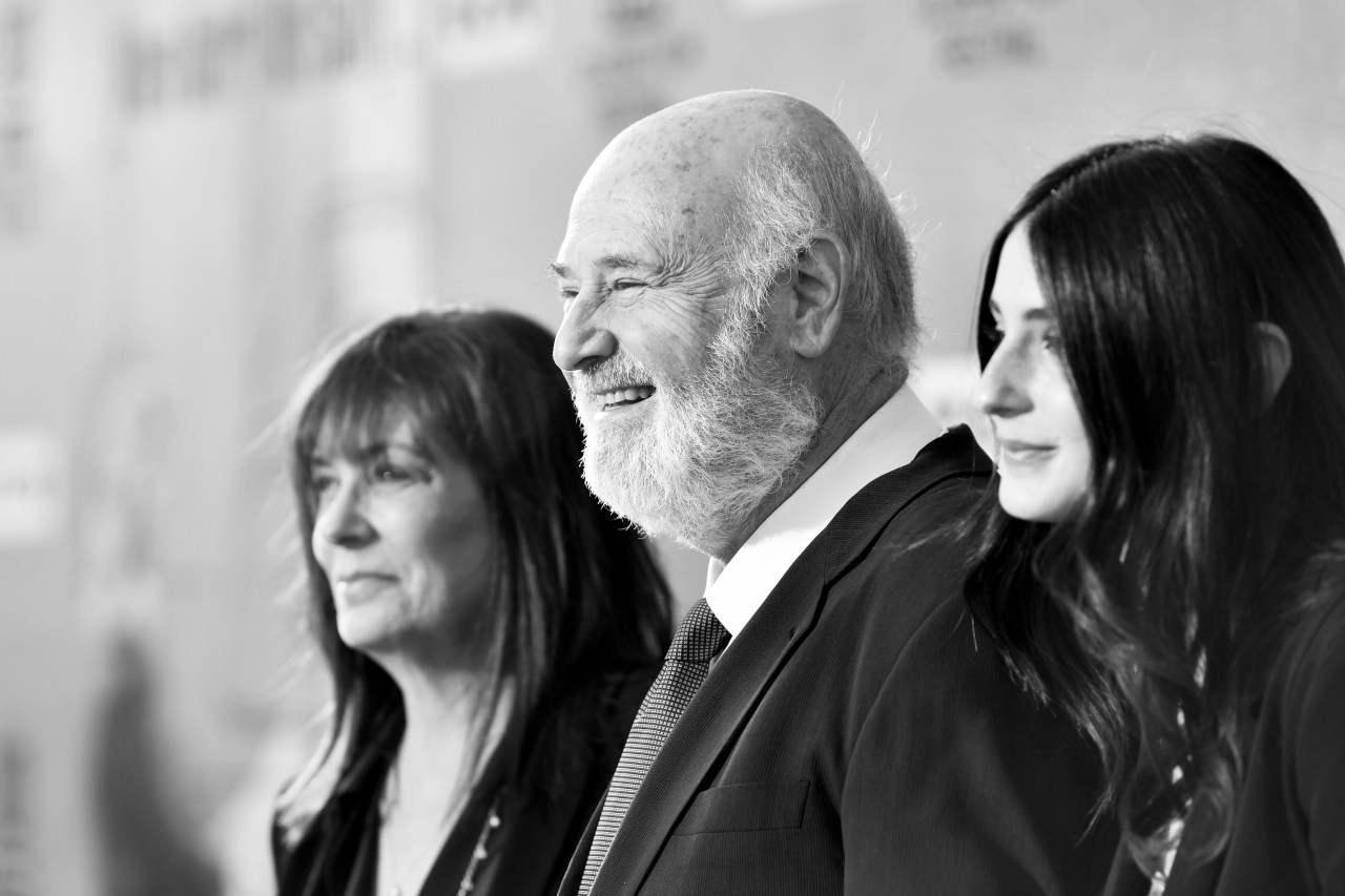 Black-and-white photo of three people in profile smiling at an event, with a step-and-repeat backdrop behind them.