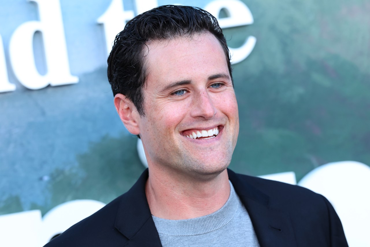 Jake Reiner smiling in a black blazer and gray shirt at an HBO premiere event in Los Angeles.