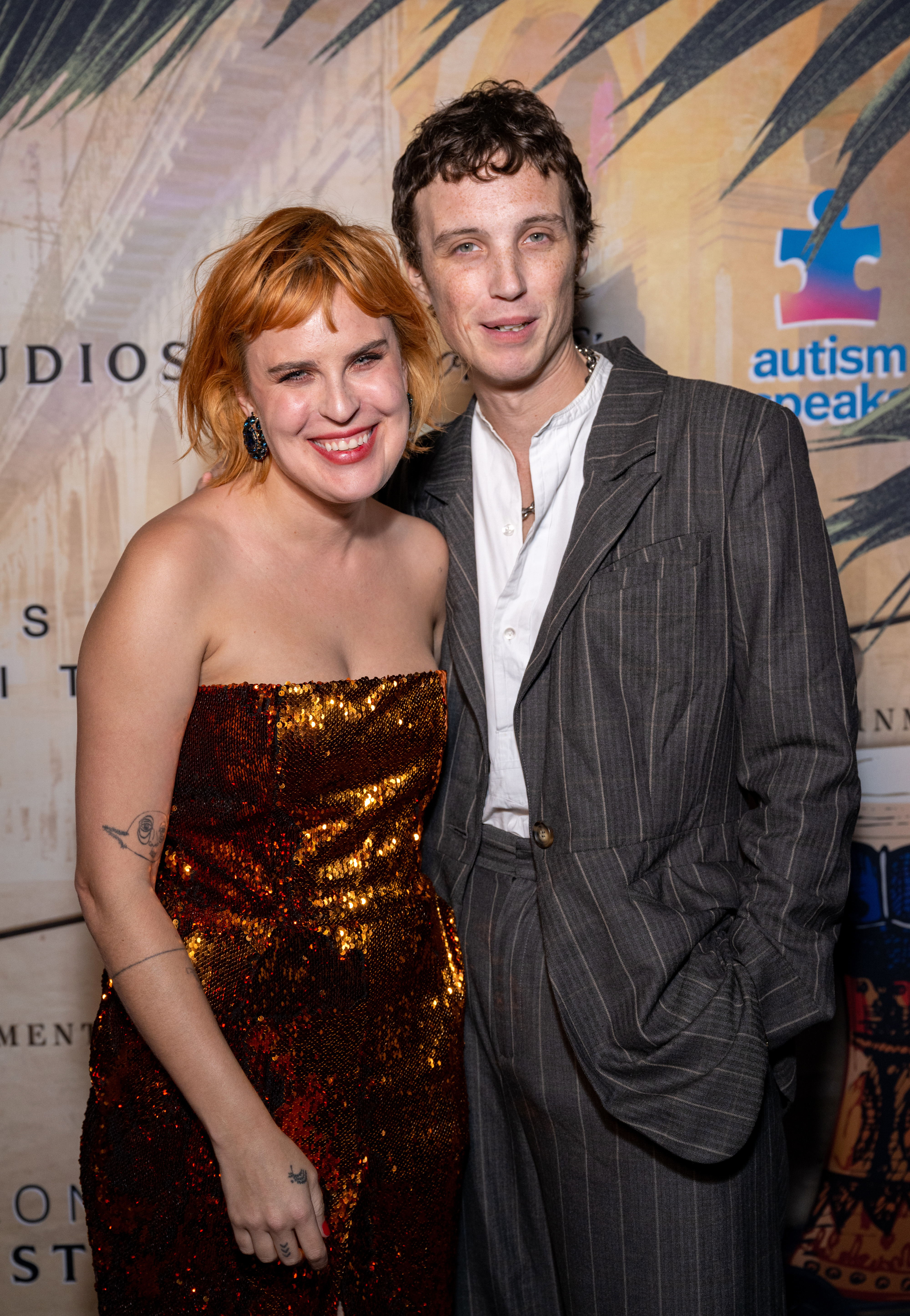 Tallulah Willis in a gold sequined strapless gown smiling beside Justin Acee in a grey pinstripe suit at an Autism Speaks event.