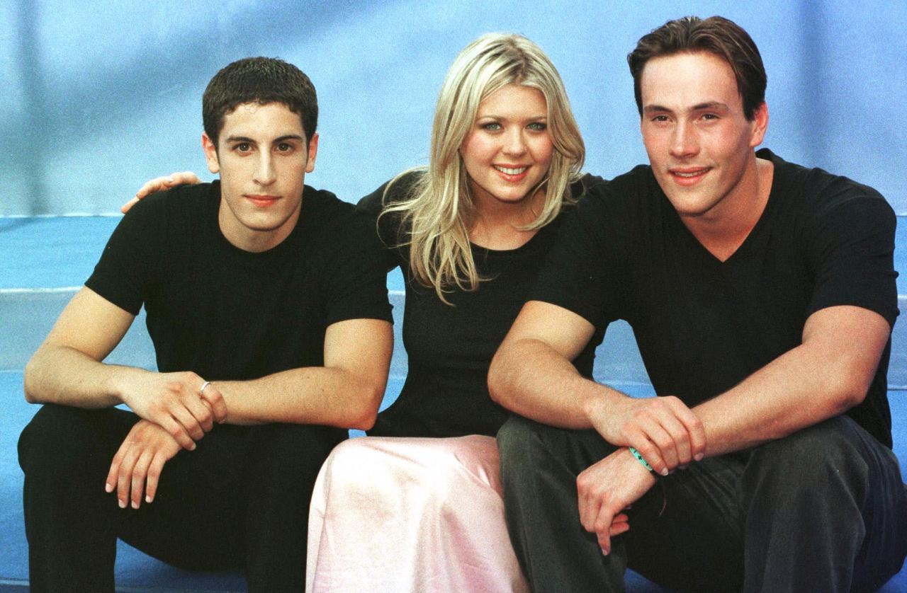 Three young actors in black outfits sit together against a blue backdrop, smiling at the camera.