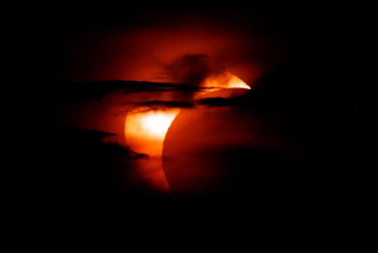 Close-up of a partial solar eclipse showing the moon's silhouette cutting across a bright orange-red sun against a black background.