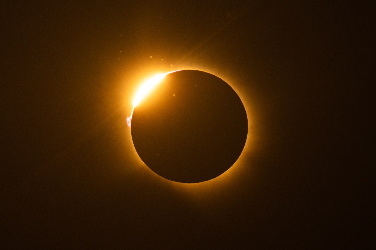 Total solar eclipse showing the moon fully blocking the sun with a bright diamond-ring flare at the upper left and a glowing corona ring