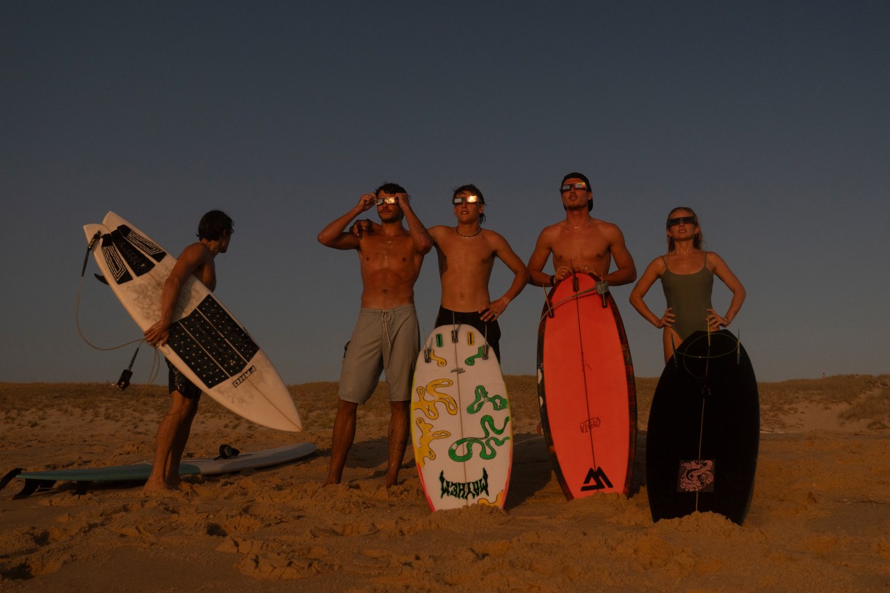 Surfers in the ocean watching a partial solar eclipse from the water off Lège-Cap-Ferret, France