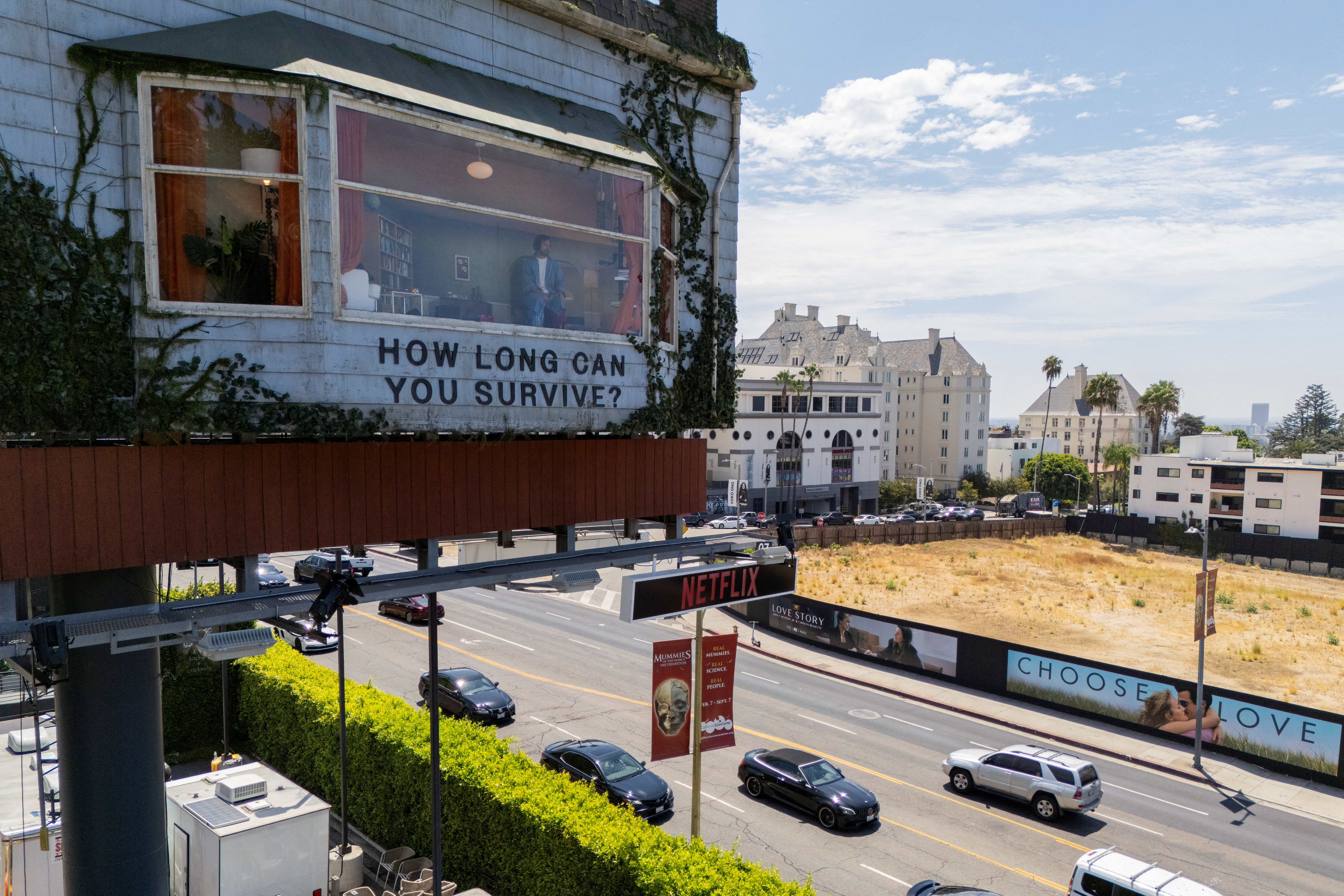 Click to open the image gallery Billboard on Sunset Boulevard shaped like a house with a man visible inside and text reading "How Long Can You Survive?" with a Netflix sign below.