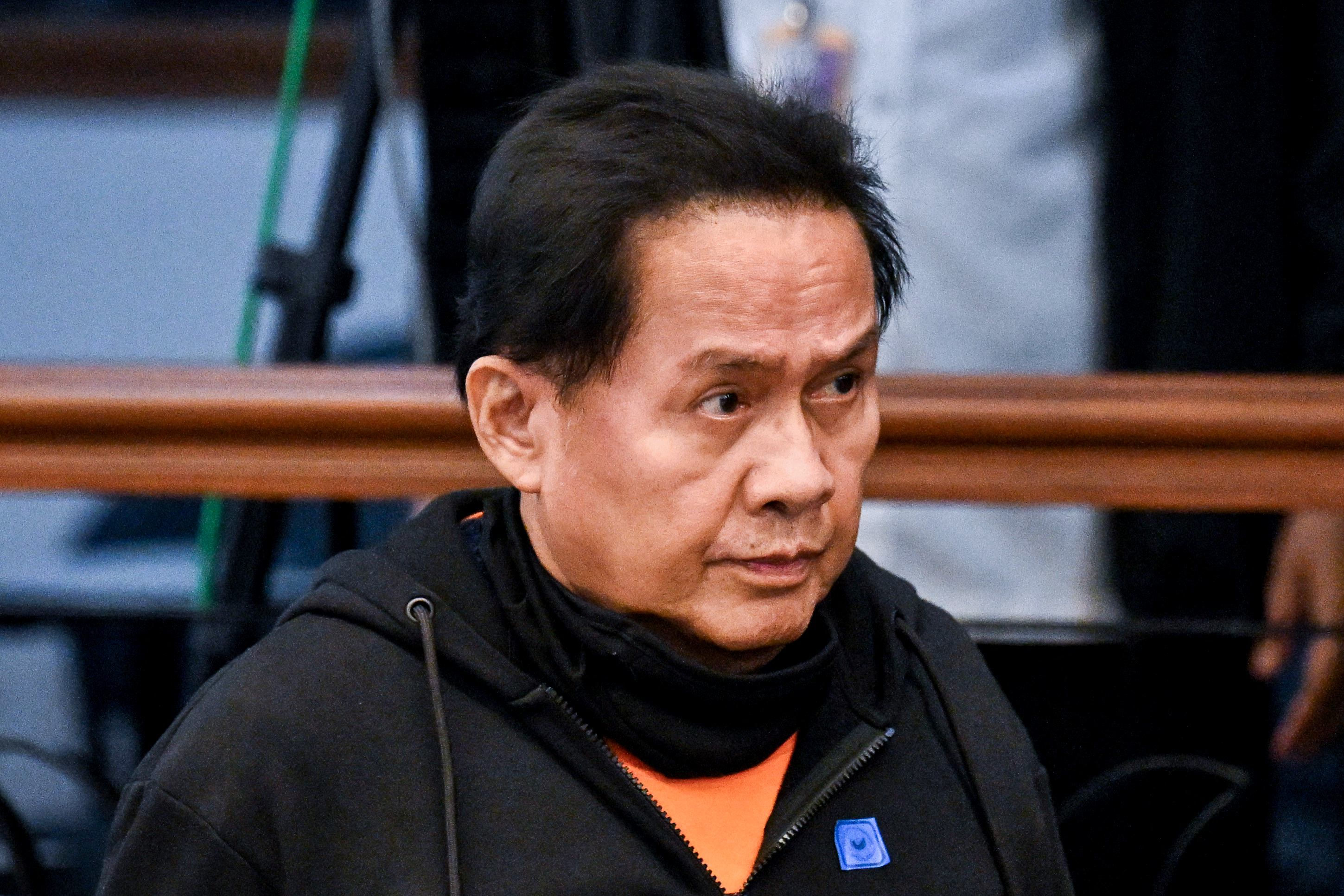 Apollo Quiboloy, wearing a black hoodie over an orange shirt, sits at a Senate hearing in Manila, looking to the side.