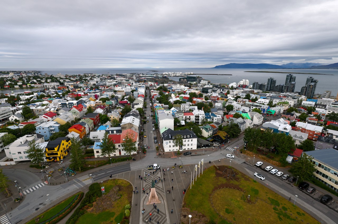 Aerial view of Reykjavik's colorful rooftops and streets stretching toward the sea, photographed from the top of Hallgrímskirkja church under a cloudy sky.