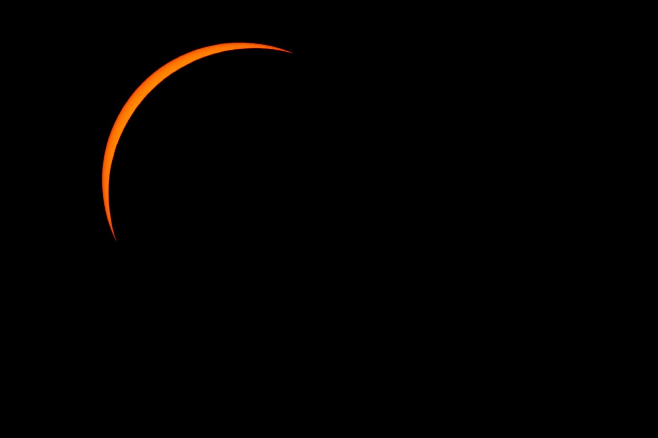 A thin crescent sliver of orange sunlight visible against a completely black sky during a near-total solar eclipse.