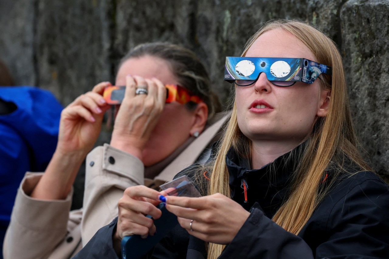 Two women wearing solar eclipse glasses look upward during the solar eclipse in Reykjavik, Iceland.