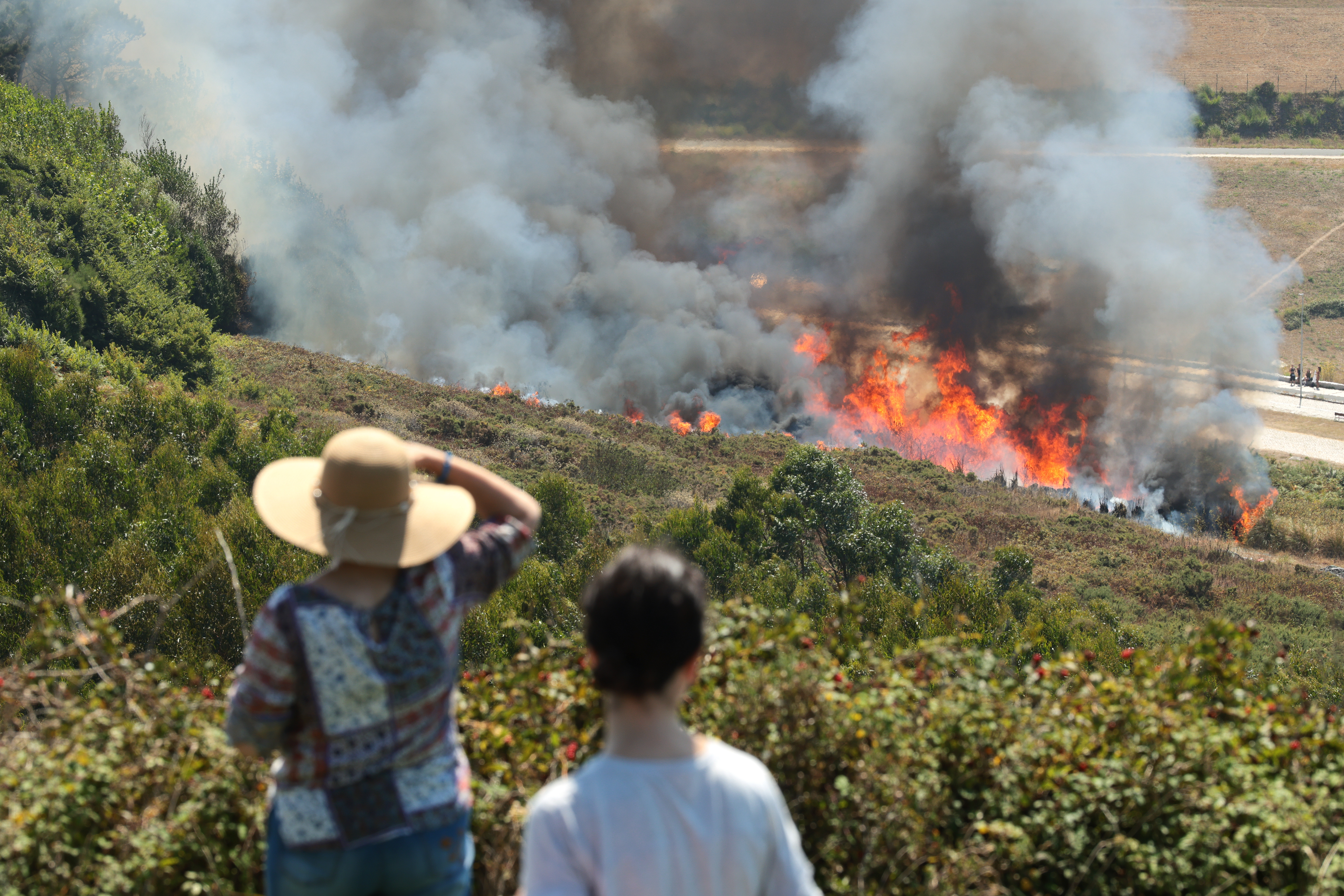 Spectators at El Monte De San Pedro park in A Coruña, Spain watch a wildfire burning on a hillside ahead of the 2026 total solar eclipse.