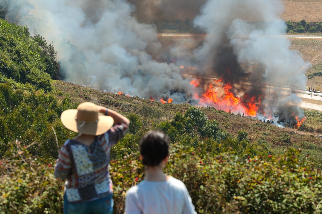 Spectators at El Monte De San Pedro park in A Coruña, Spain watch a wildfire burning on a hillside ahead of the 2026 total solar eclipse.
